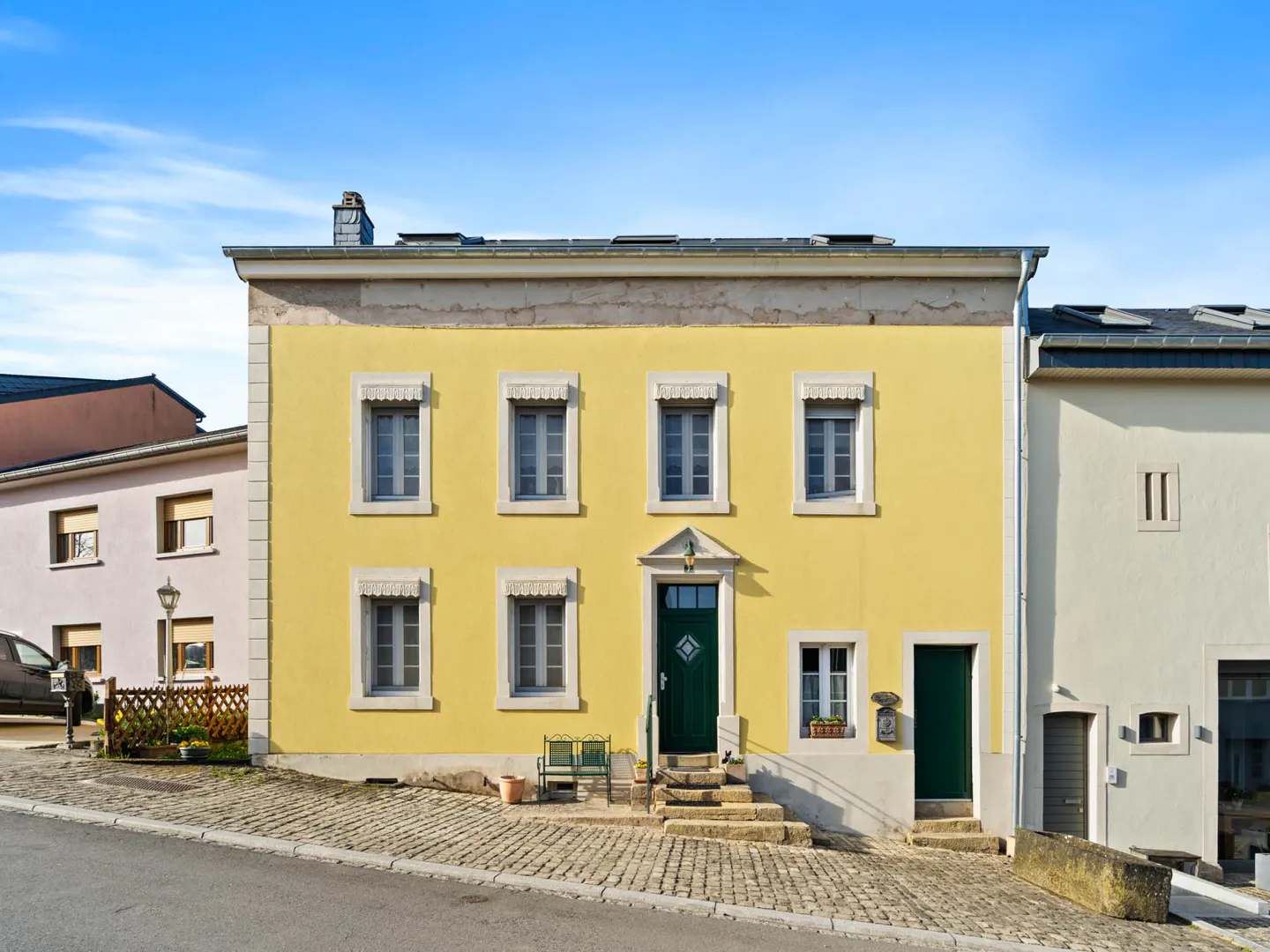 Two-story yellow house with a green door and gray windows under a blue sky.