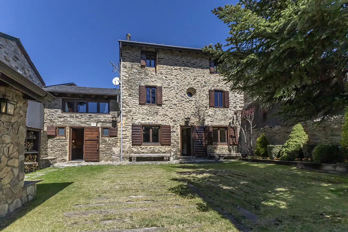 Stone house with brown shutters and a green lawn under a blue sky.