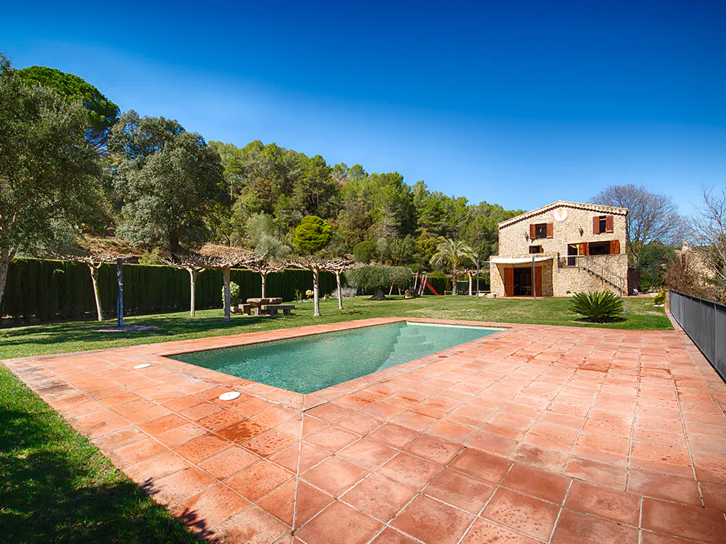 A stone house with a pool and a red tile patio on a sunny day.