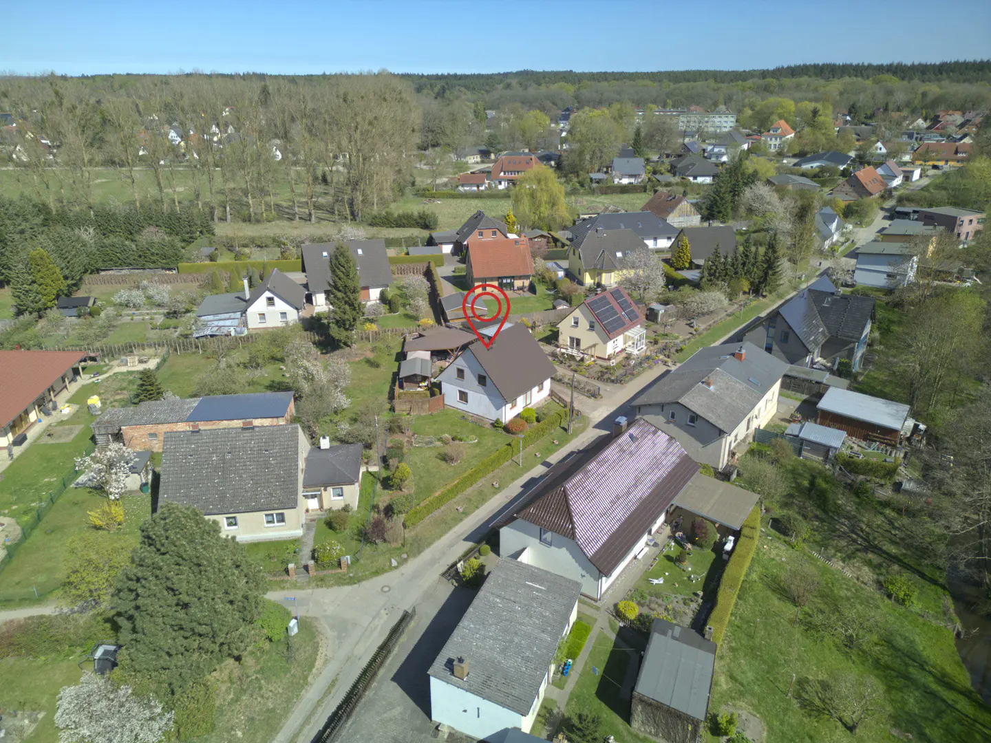 Aerial view of a small village with houses, trees, and a red location pin on a house.