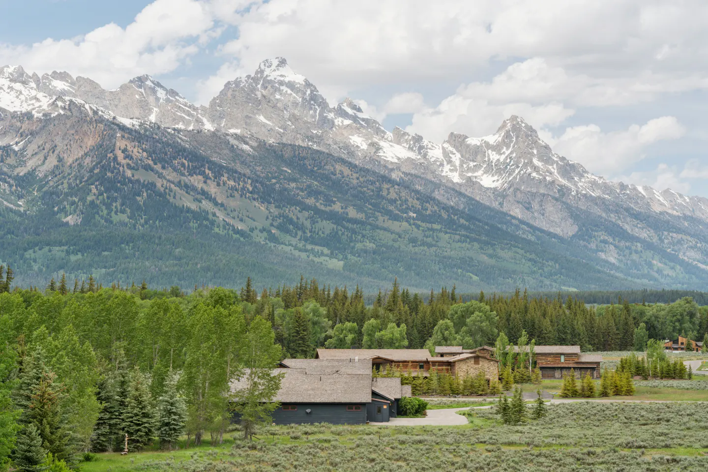 Scenic view of a property with snow-capped mountains, green trees, and a blue house.