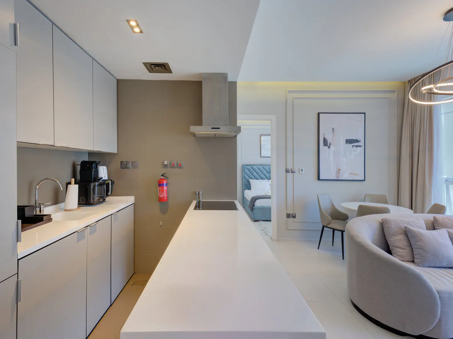 A modern apartment interior shows a kitchen with gray cabinets, a white island, and a glimpse of a bedroom and living area.