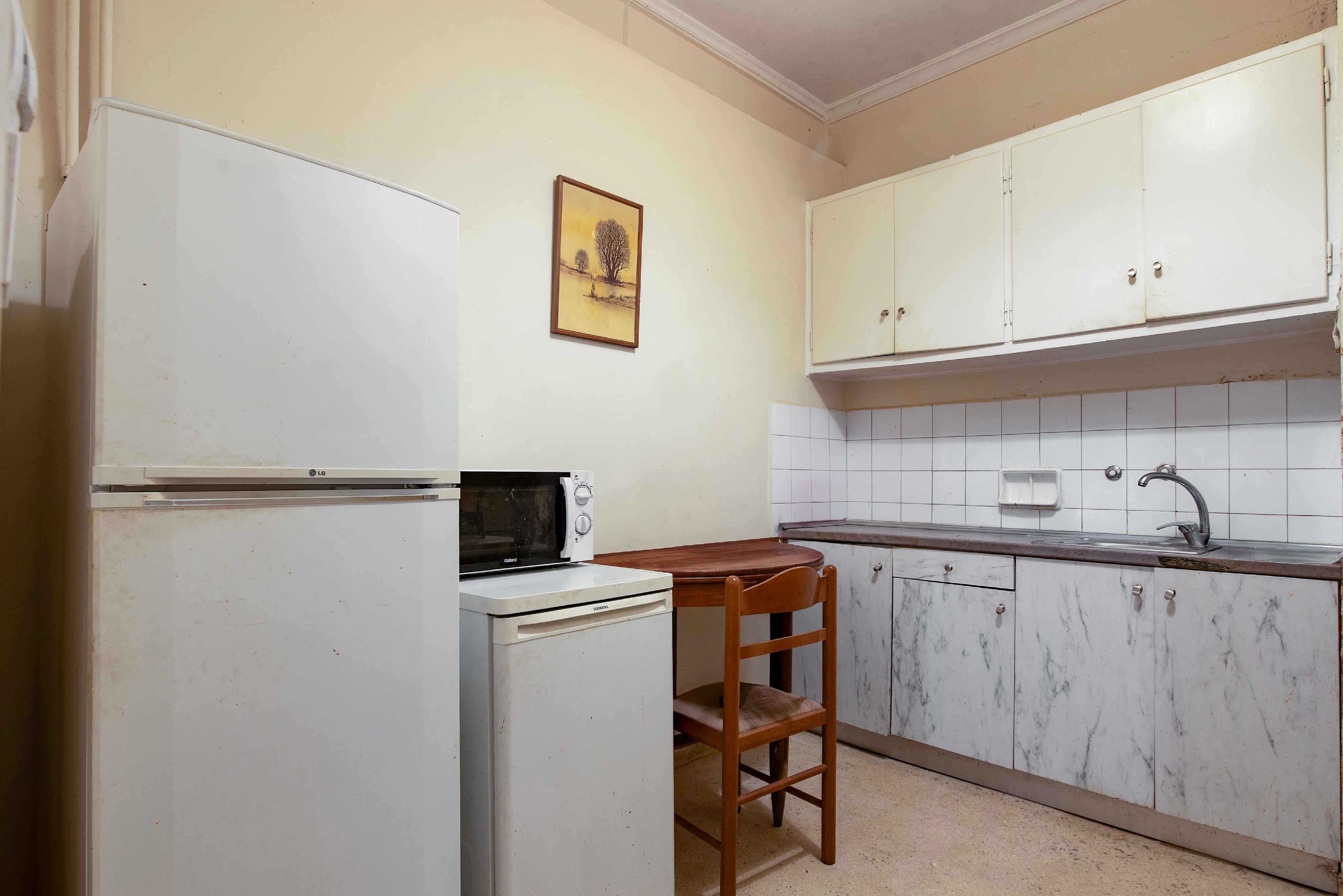 Small kitchen with white appliances, marble-patterned lower cabinets, white upper cabinets, and a small wooden dining set. [AI-generated text]