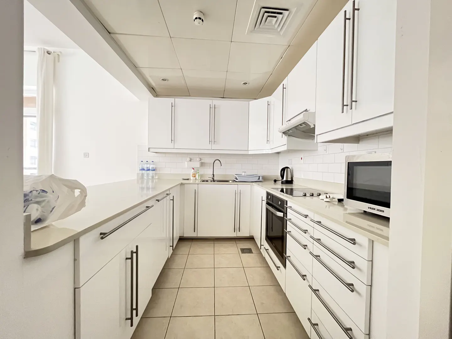 Bright, modern kitchen with white cabinets, countertops, and tile floor. Stainless steel appliances and hardware add sleek accents.