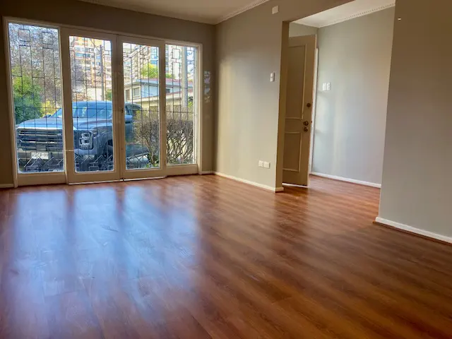 Empty living room with wood floors, beige walls, and large windows. A black truck is visible outside.