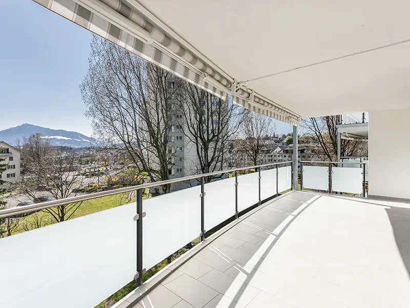 Balcony view with frosted glass railing, white tile floor, and retractable awning. Cityscape and mountain visible in the background.