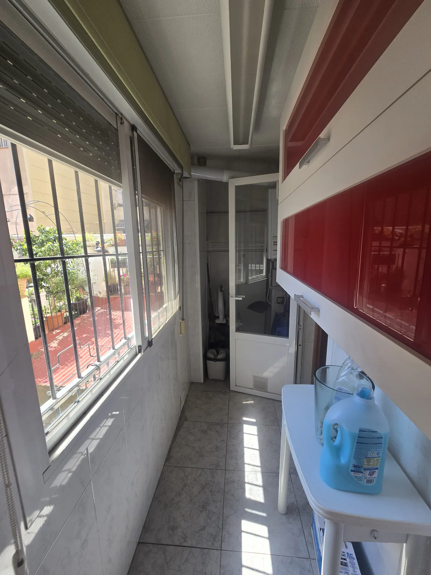 A sunroom with windows, red and white cabinets, and a white table with cleaning supplies.