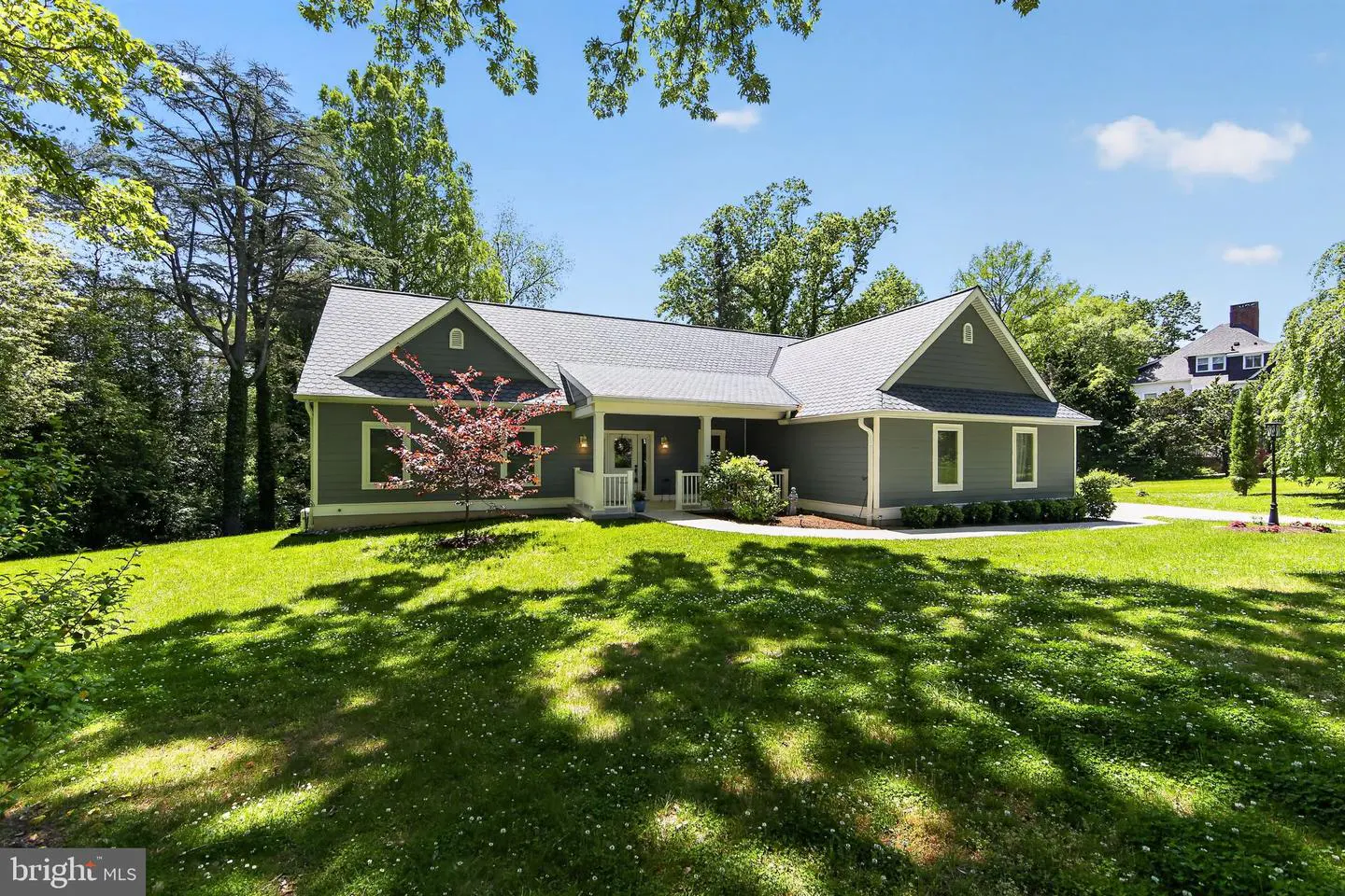 A single-story gray house with a white porch and gray roof sits on a green lawn with trees.