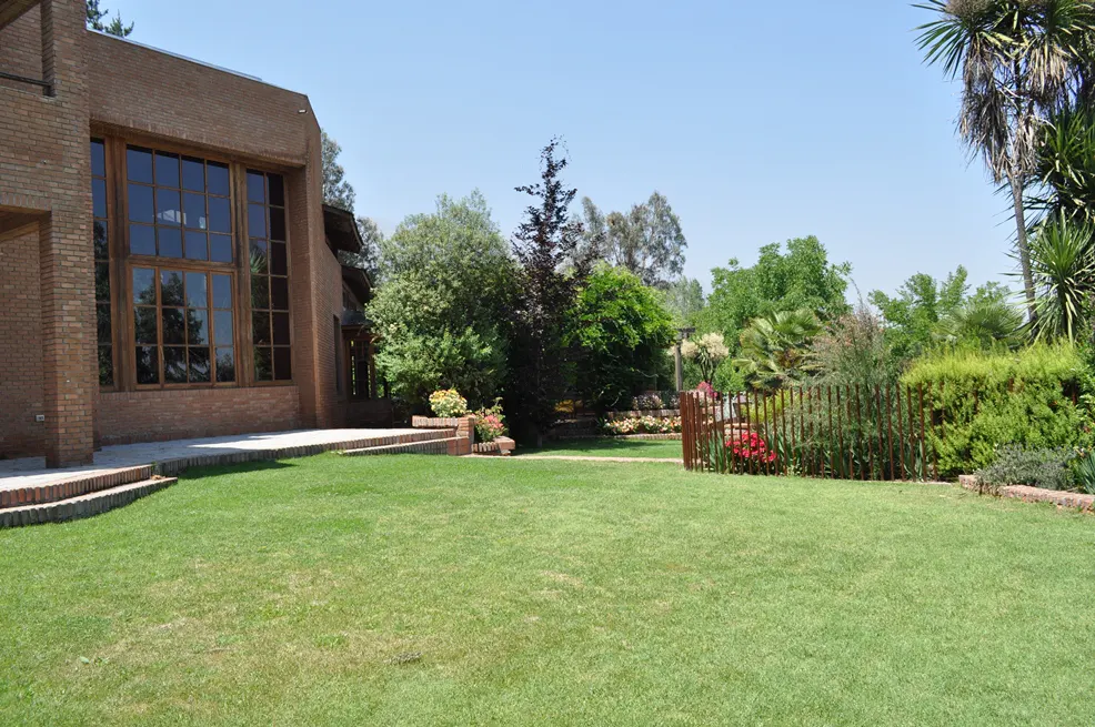 Exterior of a brick house with a large window and a green lawn, trees, and a blue sky.