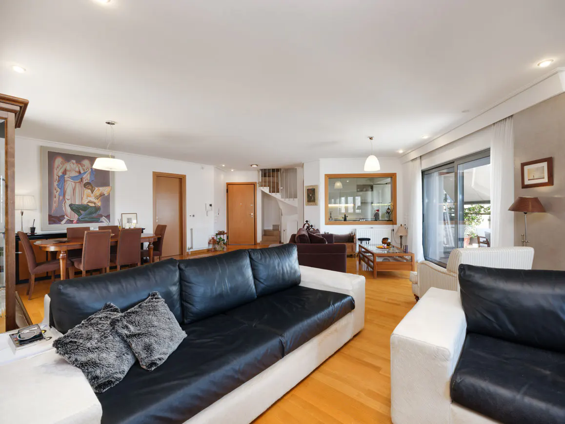 Bright, open living room with black leather sofas, wood floors, dining table, and spiral staircase in the background.