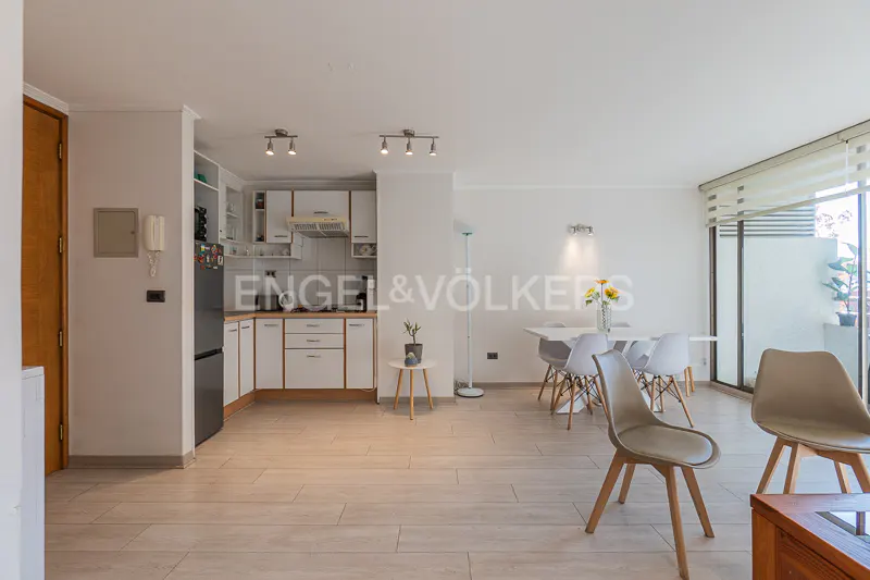 Bright, open-concept apartment with white kitchen cabinets, dining table, and balcony access. Neutral tones and natural light create a welcoming space.