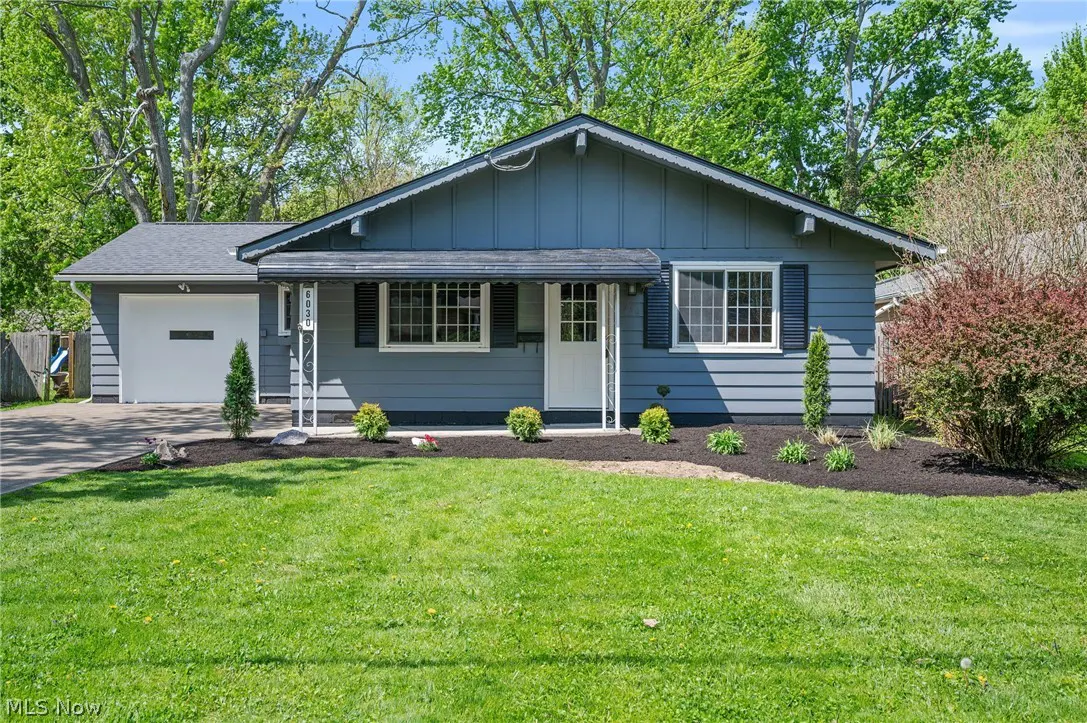 A blue single-story house with a white door and black shutters, surrounded by a green lawn and trees.