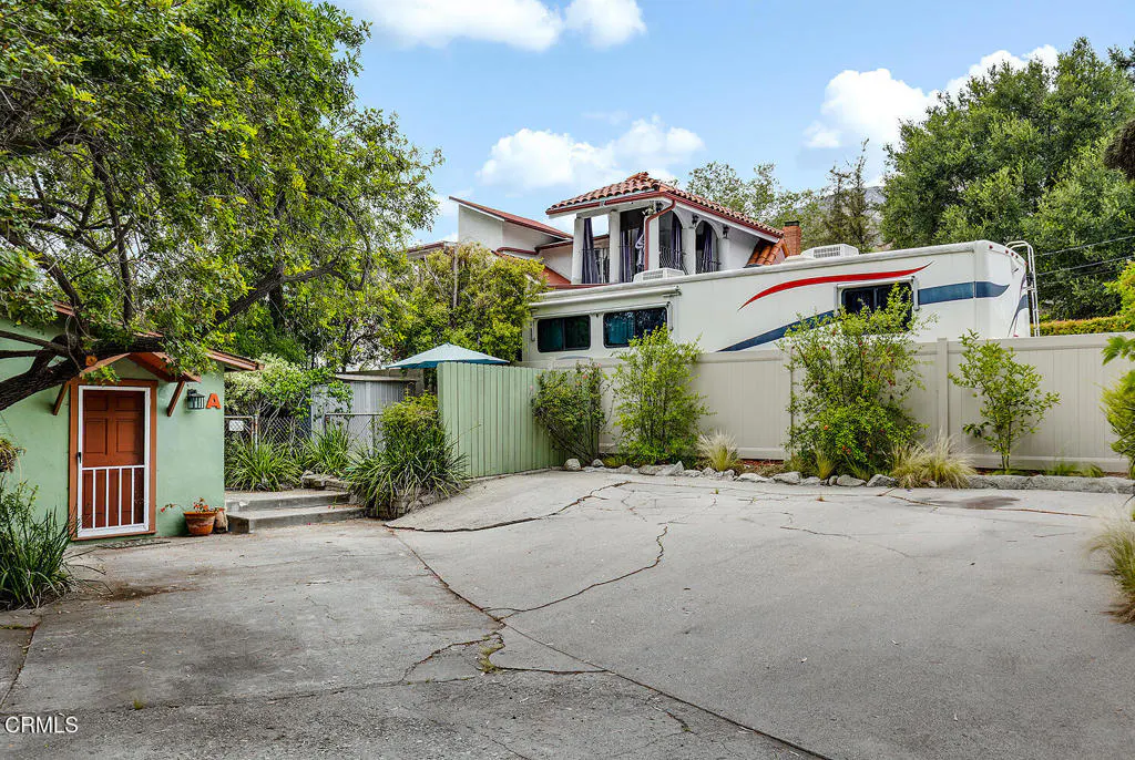 Exterior view of a property with a green shed, a white RV, and a house with a red tile roof.