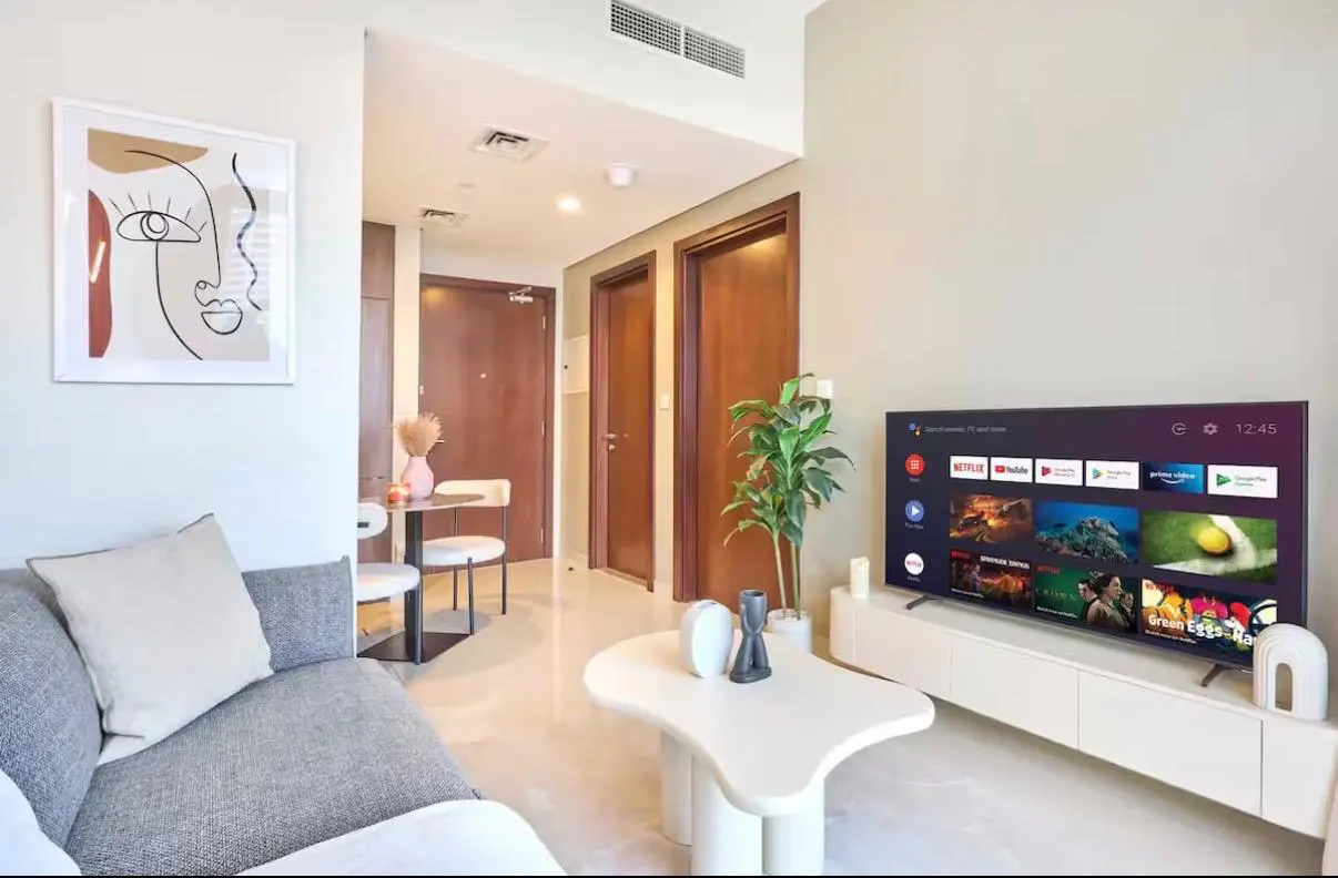 Living room with gray sofa, white coffee table, TV on a white stand, and abstract art on the wall.