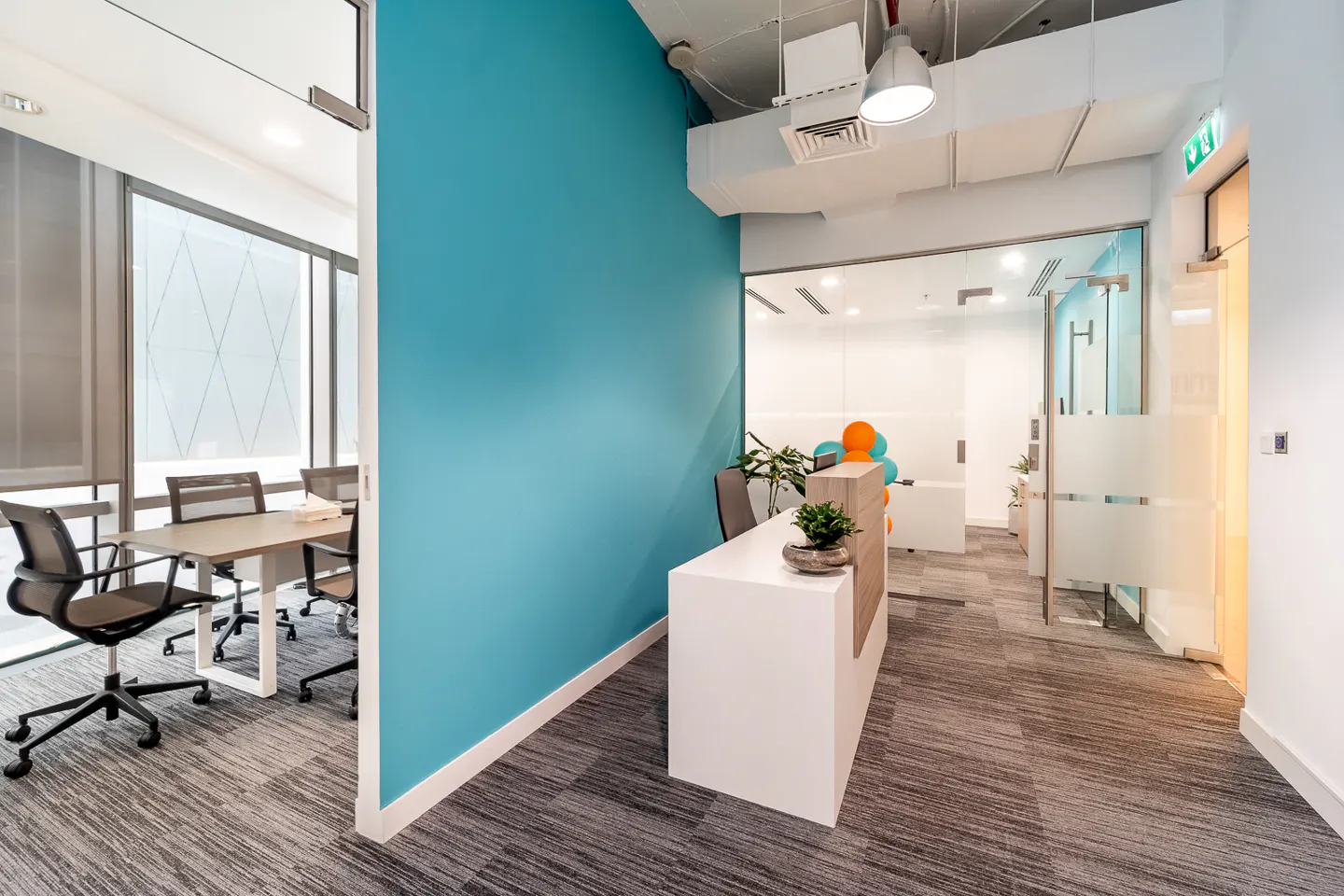 Office interior with a white reception desk, a blue accent wall, and a conference room with a table and chairs.