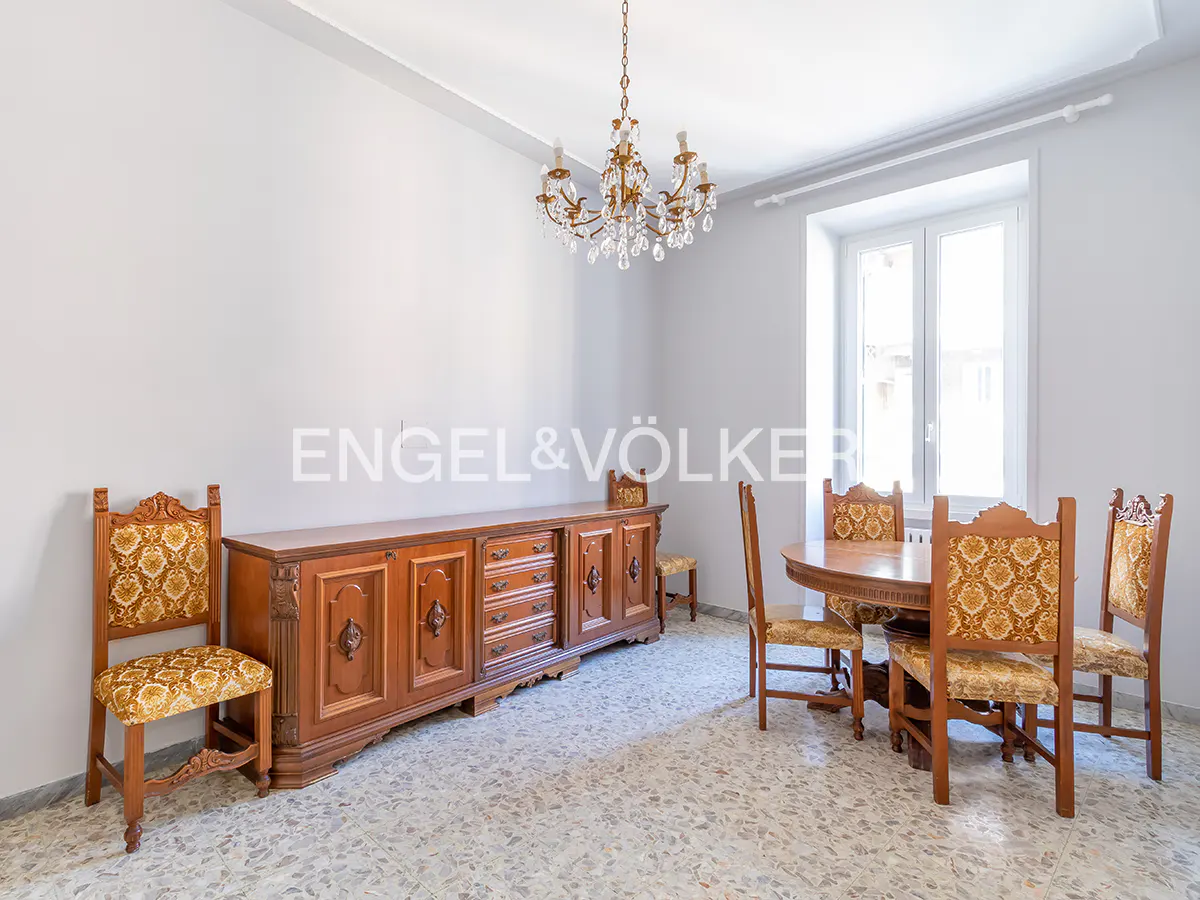 Dining room with light gray walls, terrazzo floors, a crystal chandelier, and antique wooden furniture with gold upholstery.