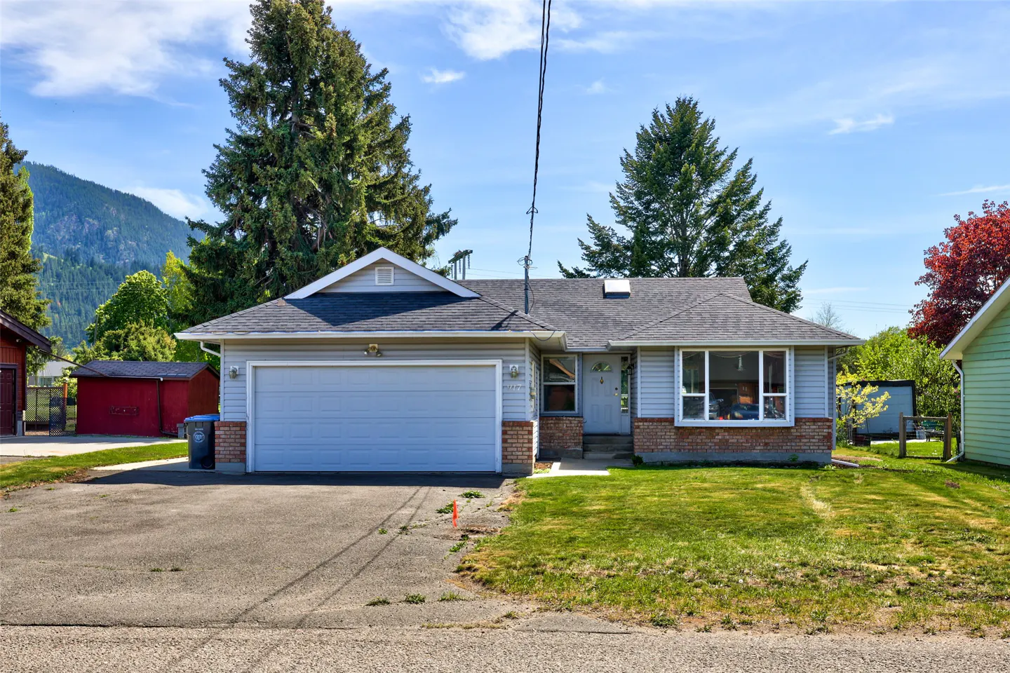 A single-story home with a gray garage door, brick accents, and a well-kept lawn on a sunny day.