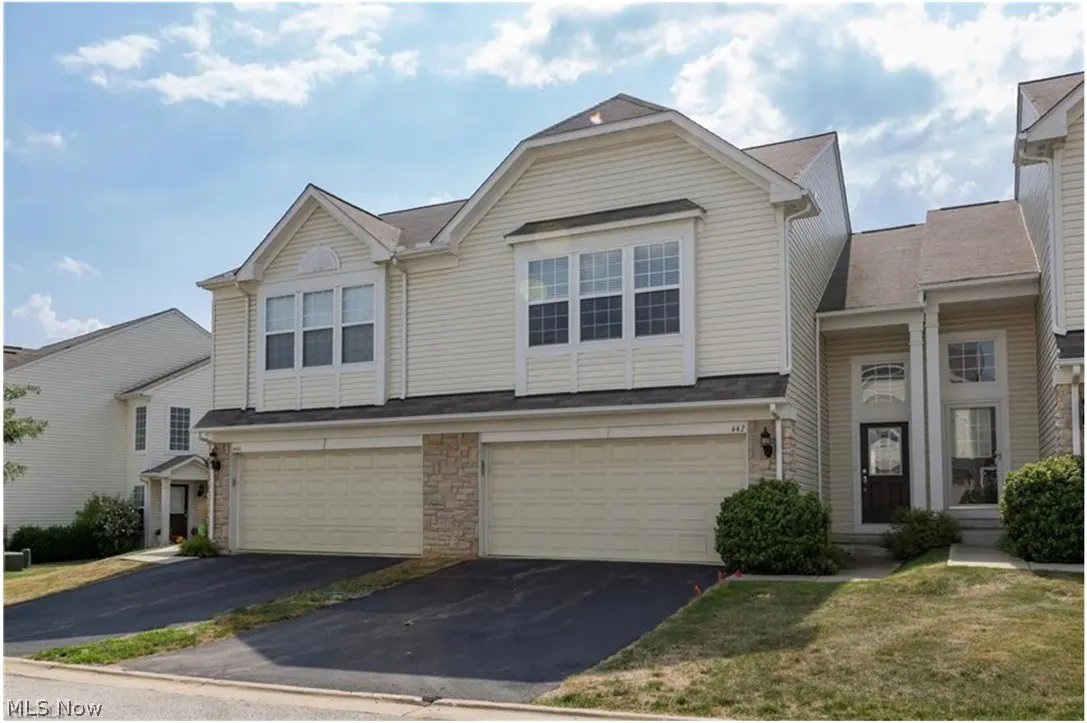 Beige two-story townhouse with two-car garage and black asphalt driveway on a sunny day.