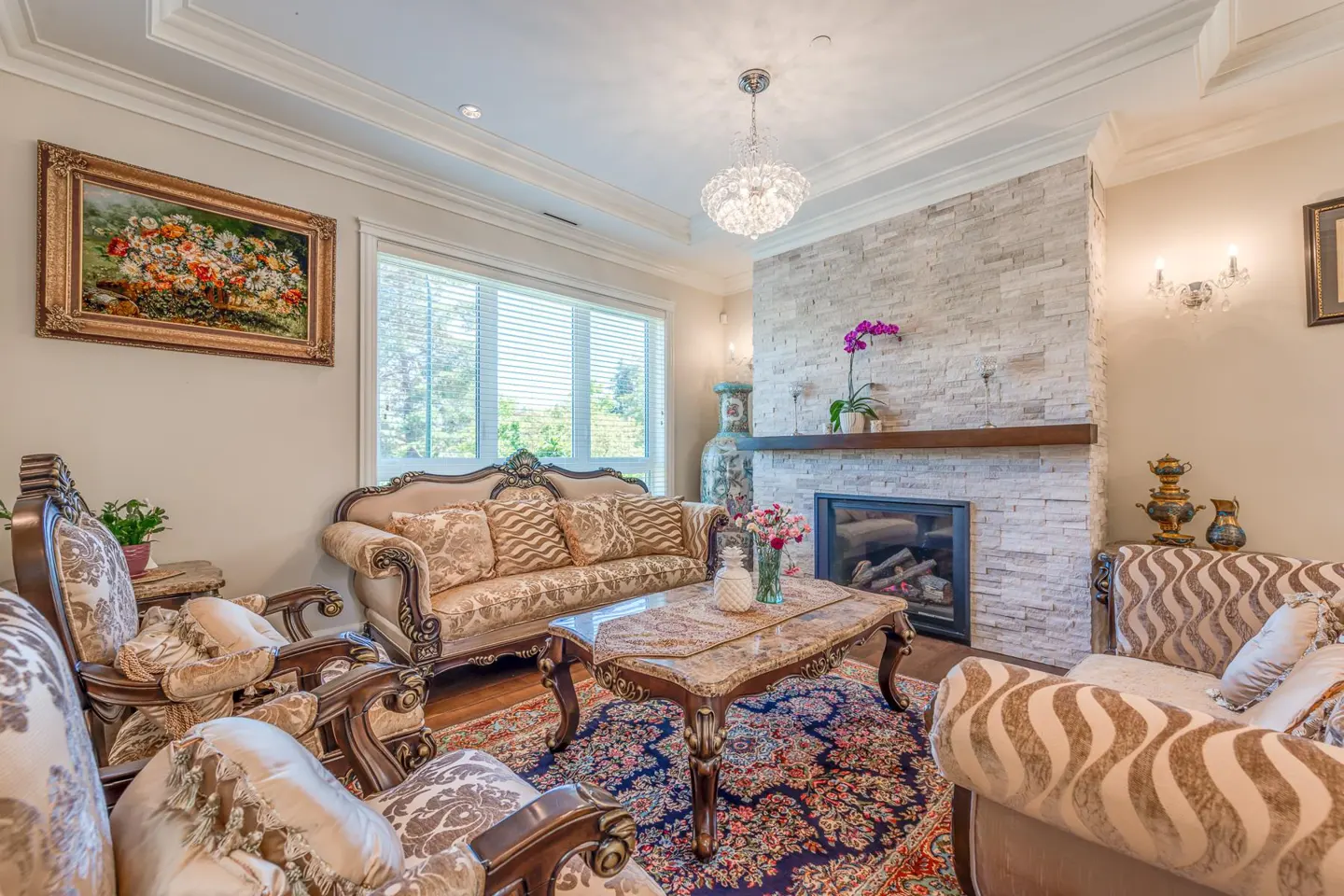 A living room with ornate furniture, a stone fireplace, and a floral rug.