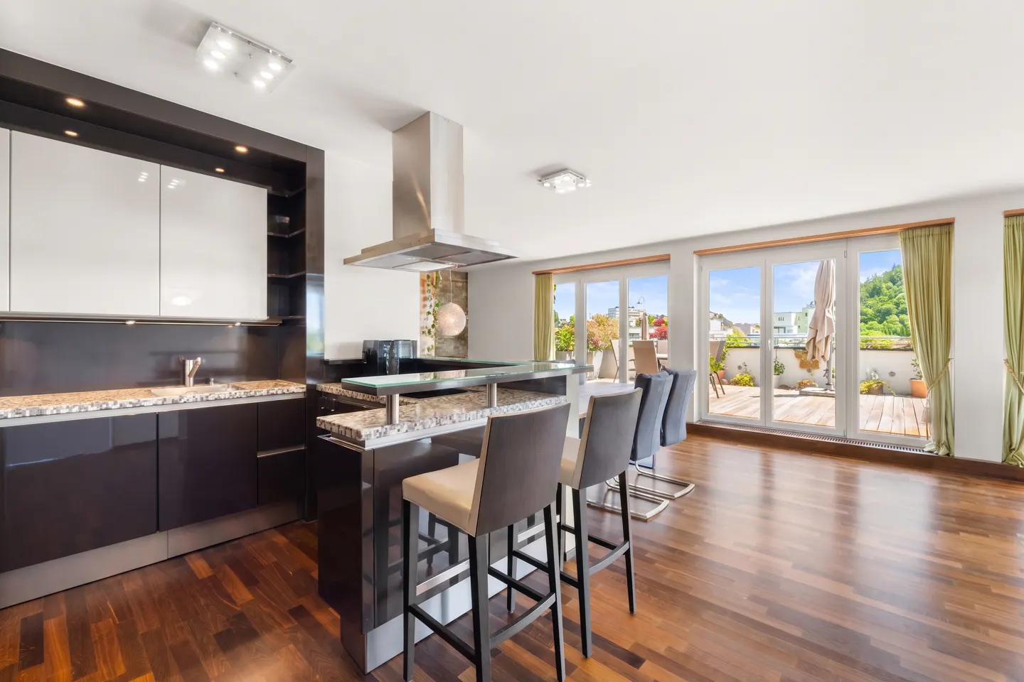 A modern kitchen with dark cabinets, a granite countertop, and a breakfast bar with stools. Sliding glass doors lead to a terrace.