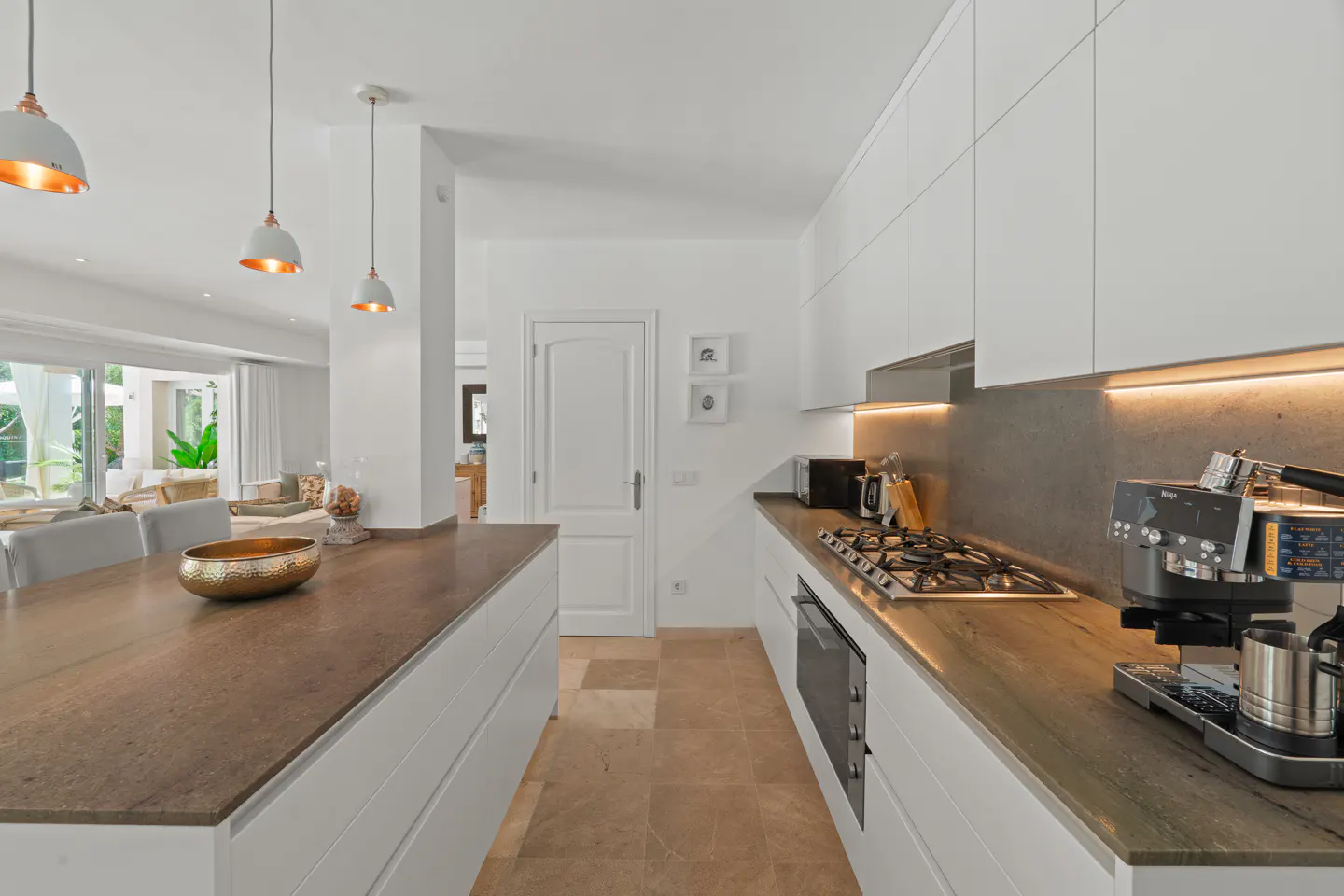 A modern kitchen with white cabinets, brown countertops, and stainless steel appliances. Pendant lights hang over the island.