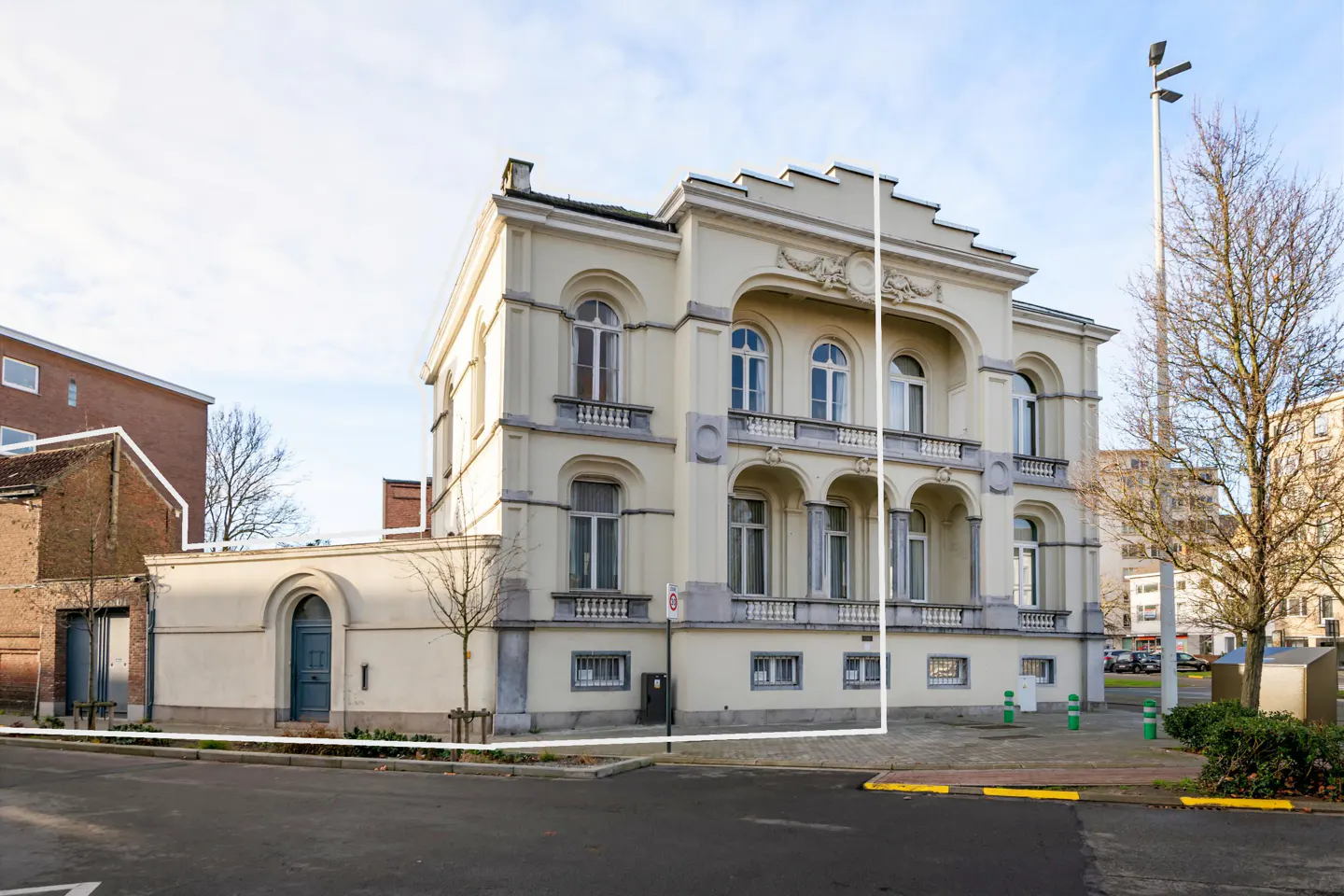 Exterior view of a three-story, light yellow building with arched windows and a balcony, next to a brick building.