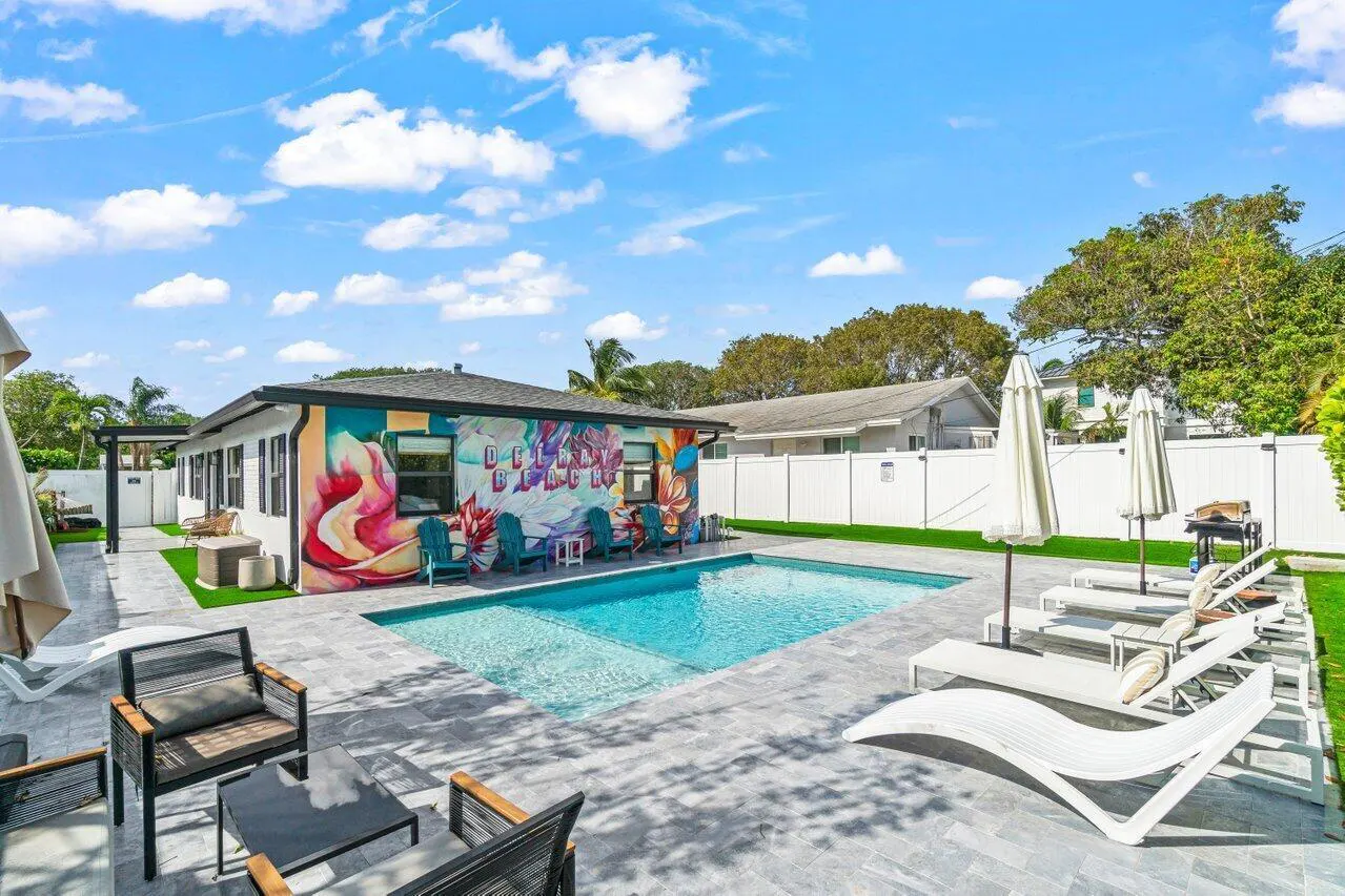 Outdoor pool area with lounge chairs and seating. Building with mural that says "Delray Beach" in the background.