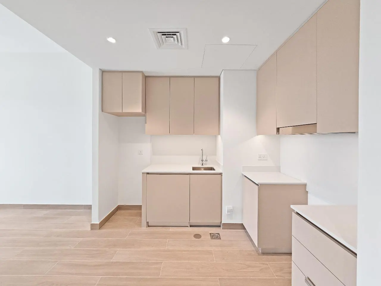 Bright, modern kitchen with light wood floors and beige cabinets. White countertops and walls create a clean, minimalist aesthetic.