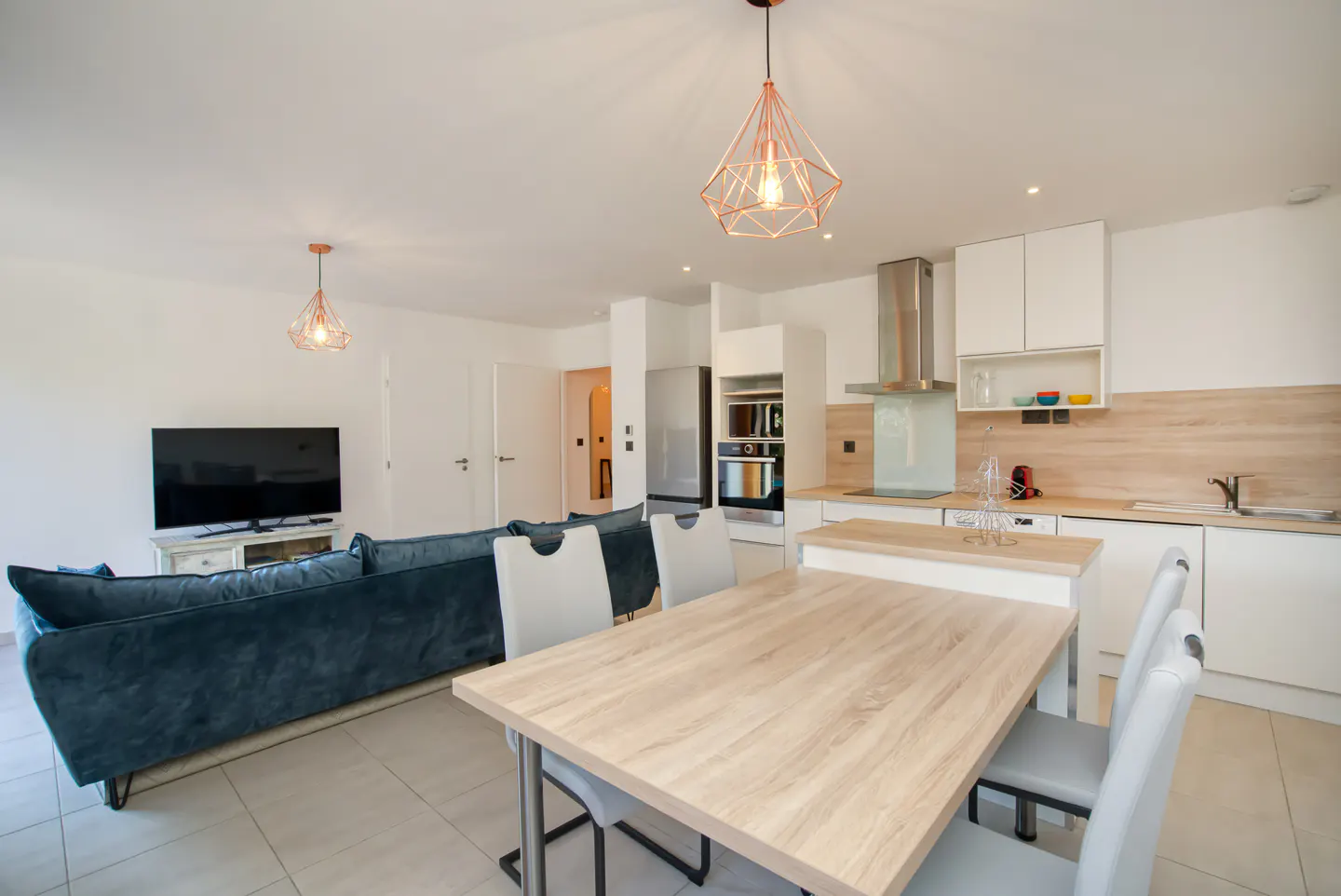 Open-concept living space with a blue sofa, wood table with chairs, and a white kitchen with stainless steel appliances.
