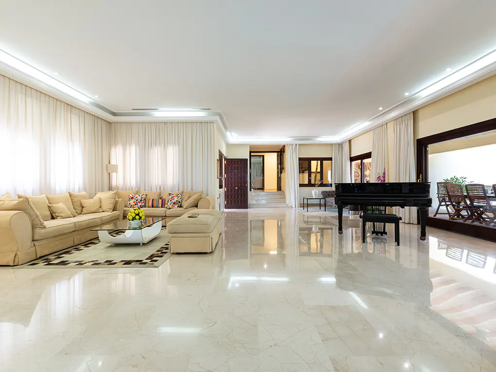 Bright, spacious living room with beige sofa, glass table, and black grand piano on a marble floor.