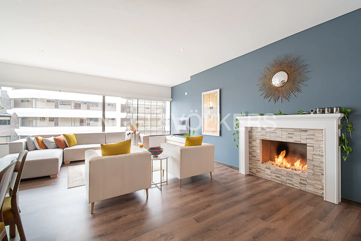 Living room with a fireplace, hardwood floors, and a large window. The walls are blue and there is a white sofa and two chairs.