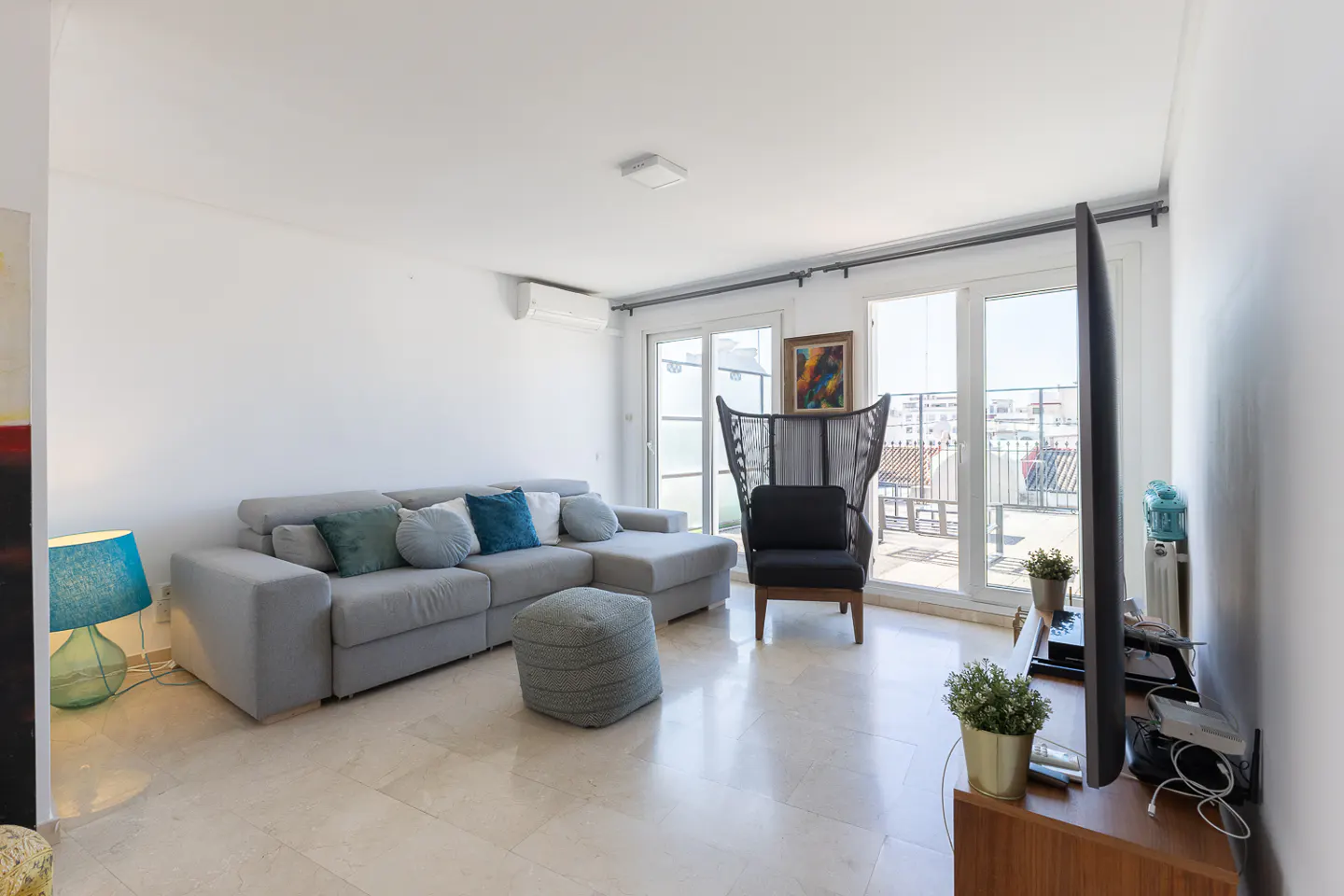 Bright living room with a gray sectional sofa, blue pillows, and a unique high-backed chair near sliding glass doors to a balcony.