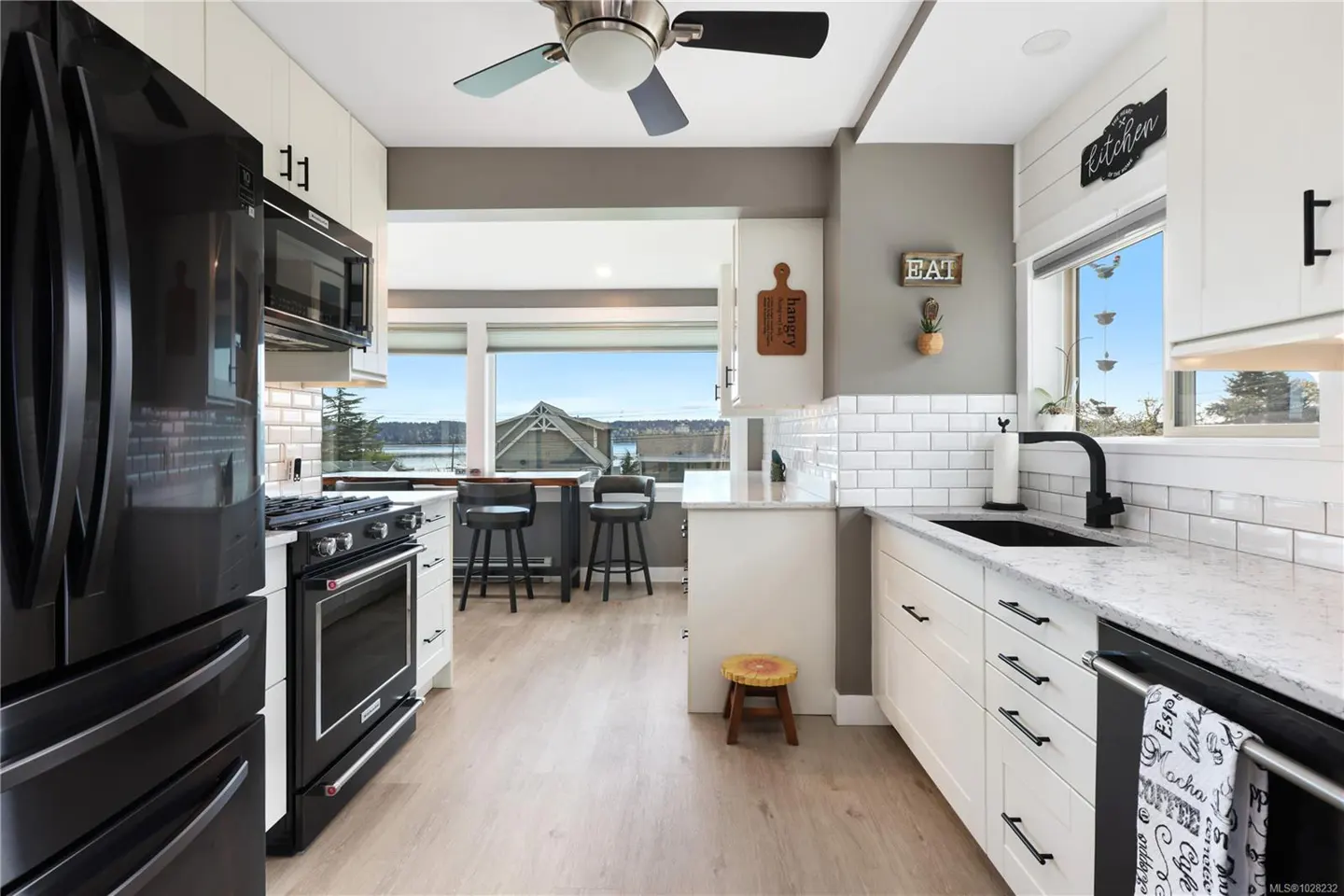 Bright kitchen with white cabinets, black appliances, and a view of the water. A ceiling fan hangs above.