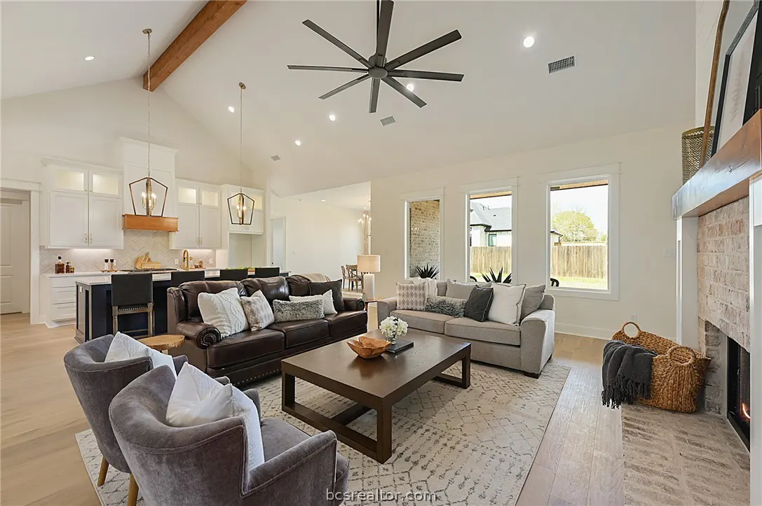 Open-concept living room with vaulted ceilings, dark leather and grey sofas, a wood coffee table, and a brick fireplace.