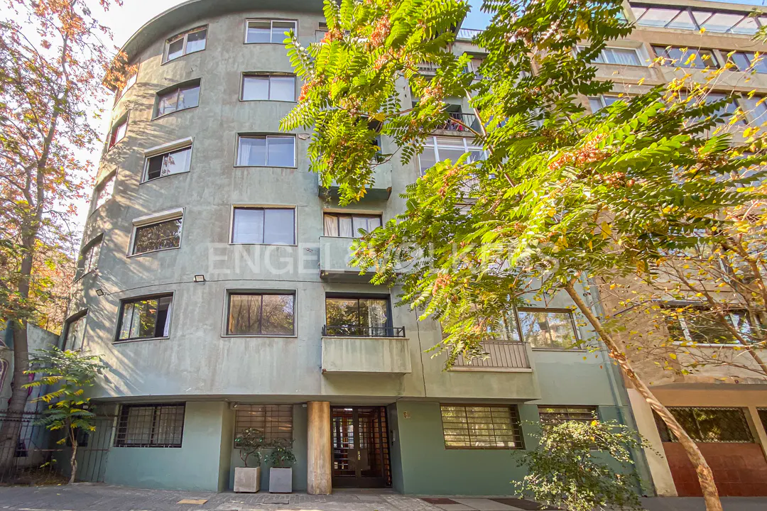 Exterior of a multi-story, curved, light green apartment building with many windows and trees in front.