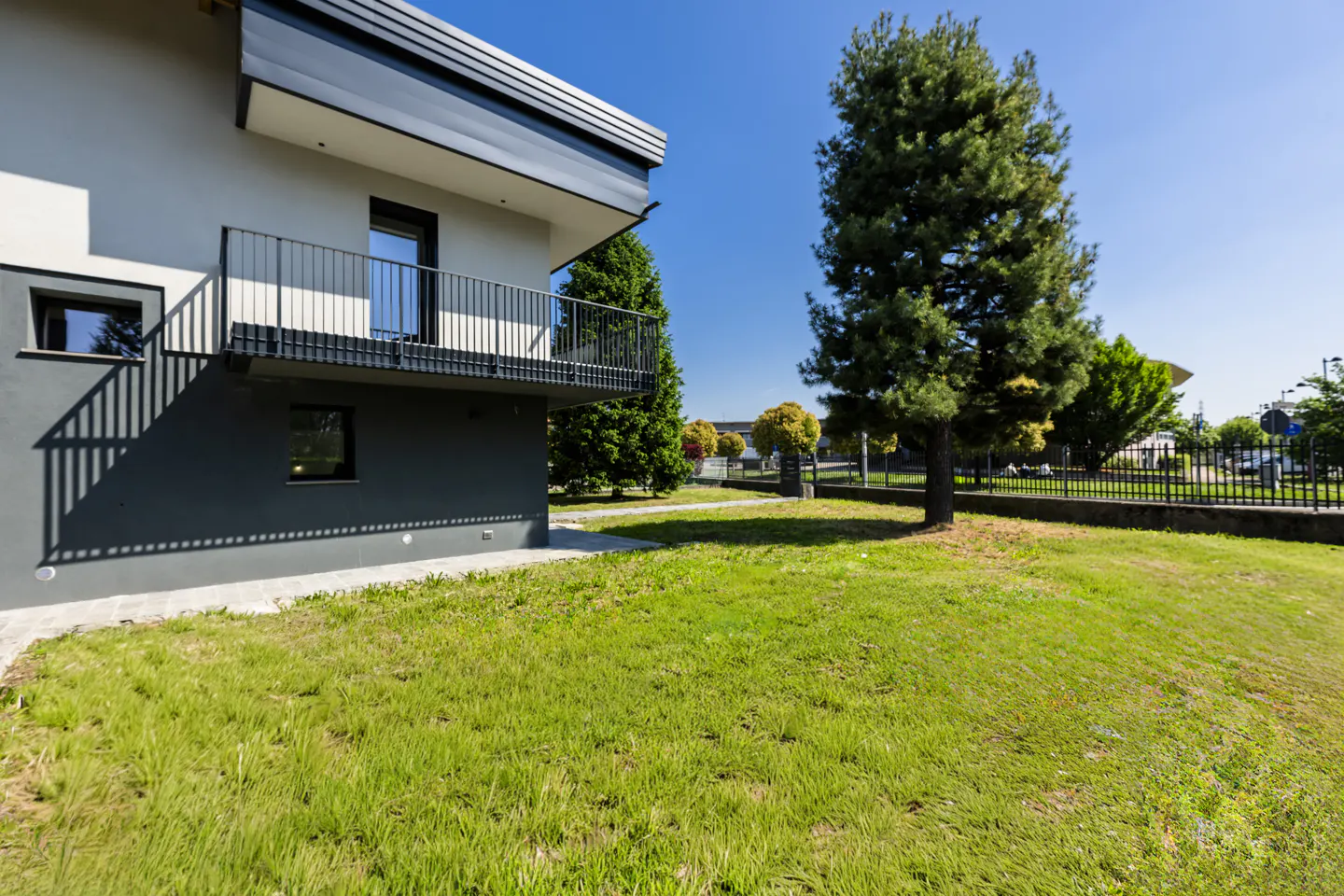 Modern two-story house with a gray balcony and a green lawn under a clear blue sky.