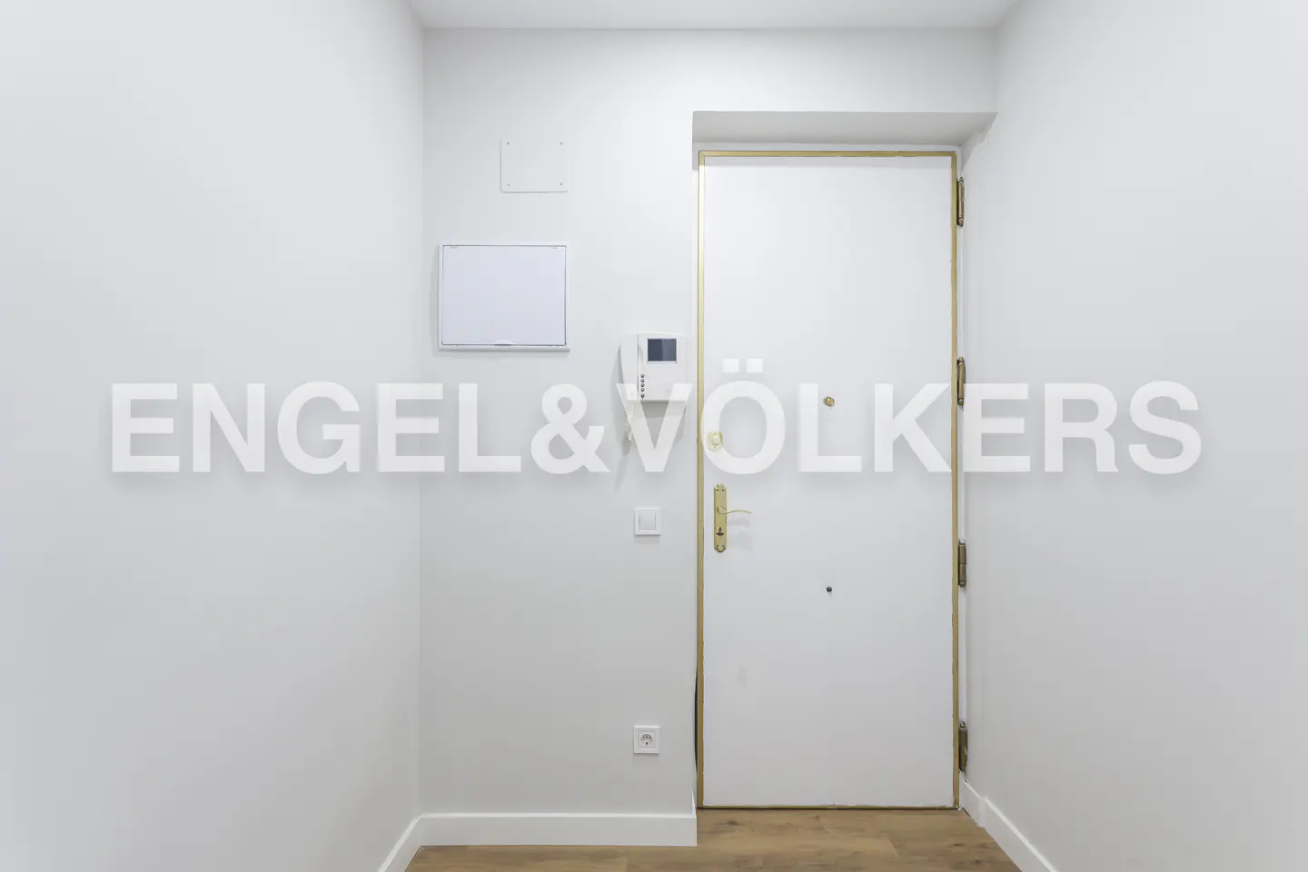 Entryway with white walls, light wood floors, and a white door with gold trim. Intercom system and electrical panels are visible. "Engel & Völkers" logo overlay.