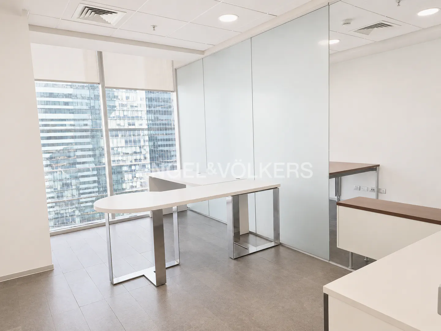 Bright office space with white desks, steel legs, and a frosted glass wall. A large window shows a city view.