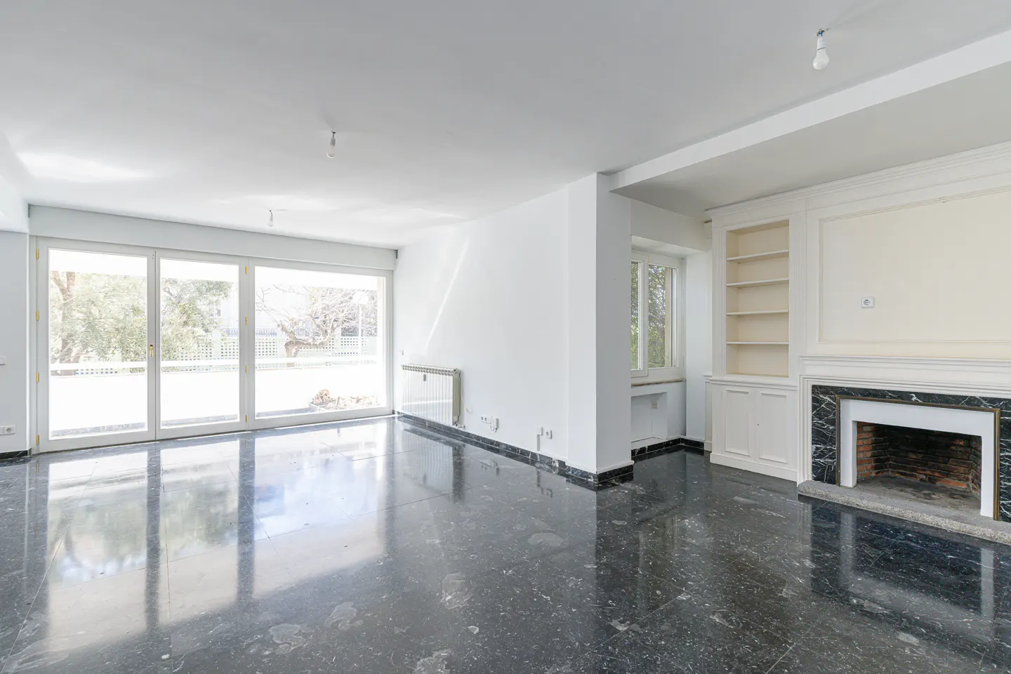 Bright, empty room with white walls, black marble floor, fireplace, and large sliding glass doors to the outside.