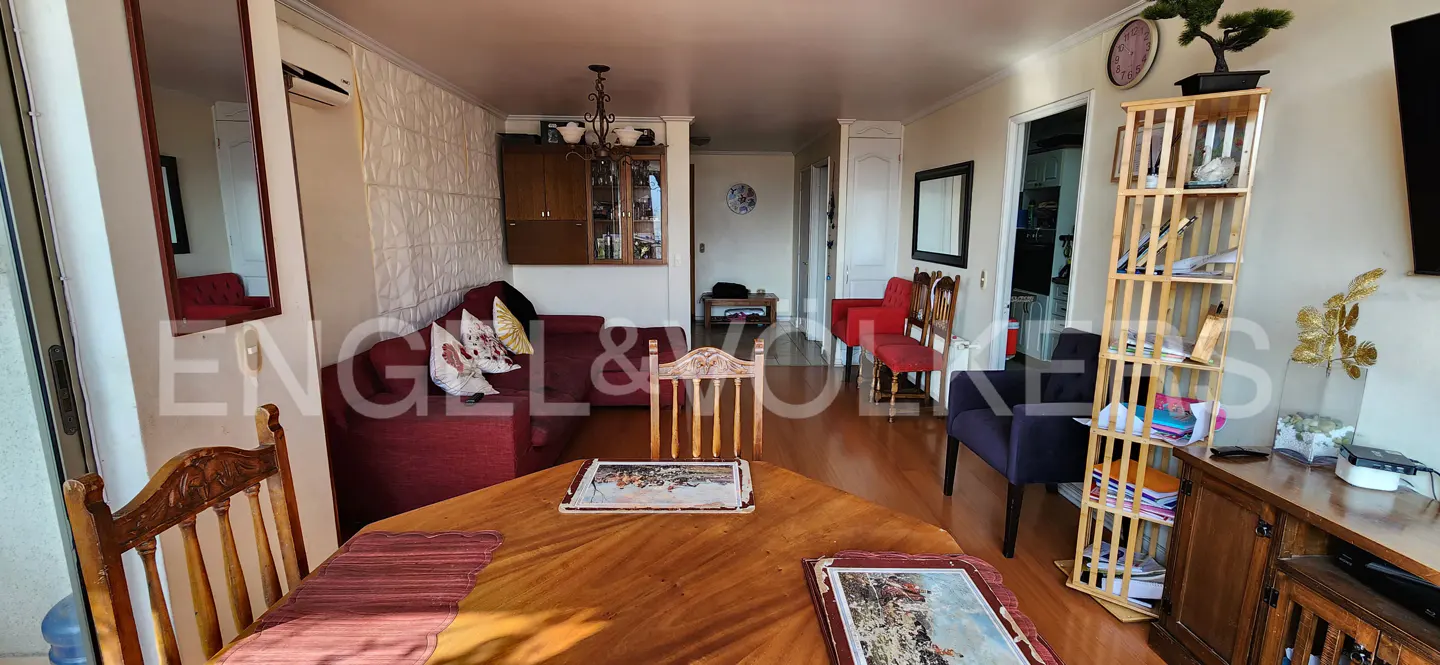 A living room with a wooden table, red sofa, and a bookshelf. The room has hardwood floors and natural light.