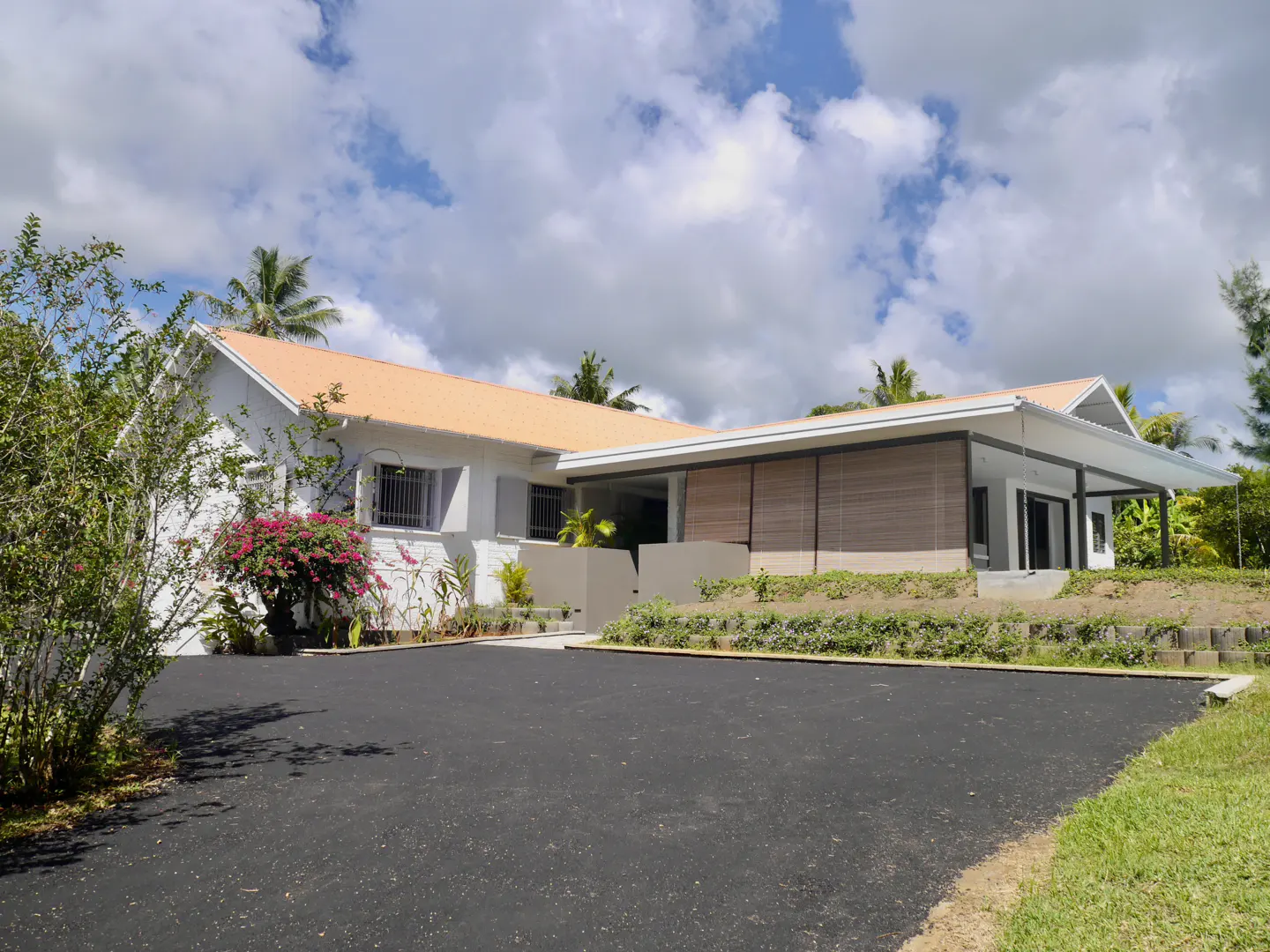 A white, single-story house with an orange roof and a black driveway on a sunny day.