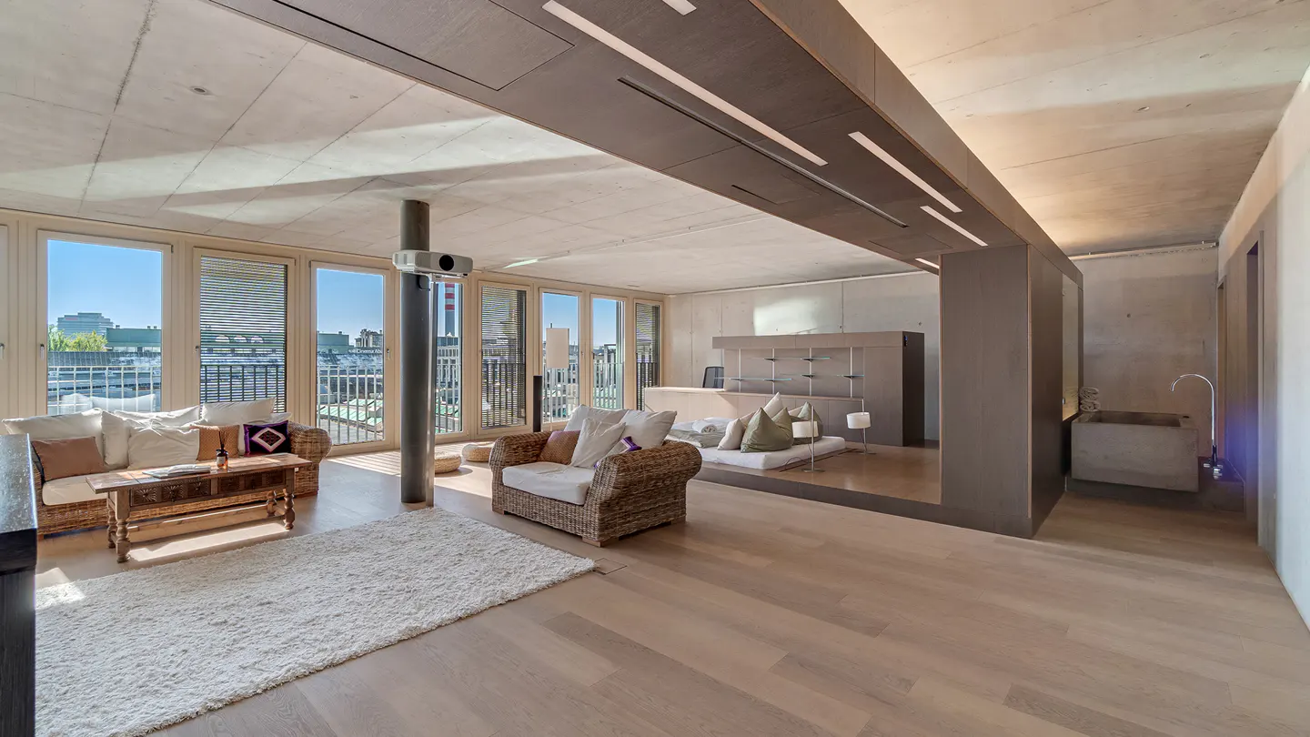 Bright, modern living room with wicker furniture, a projector, and a view of the city through large windows.