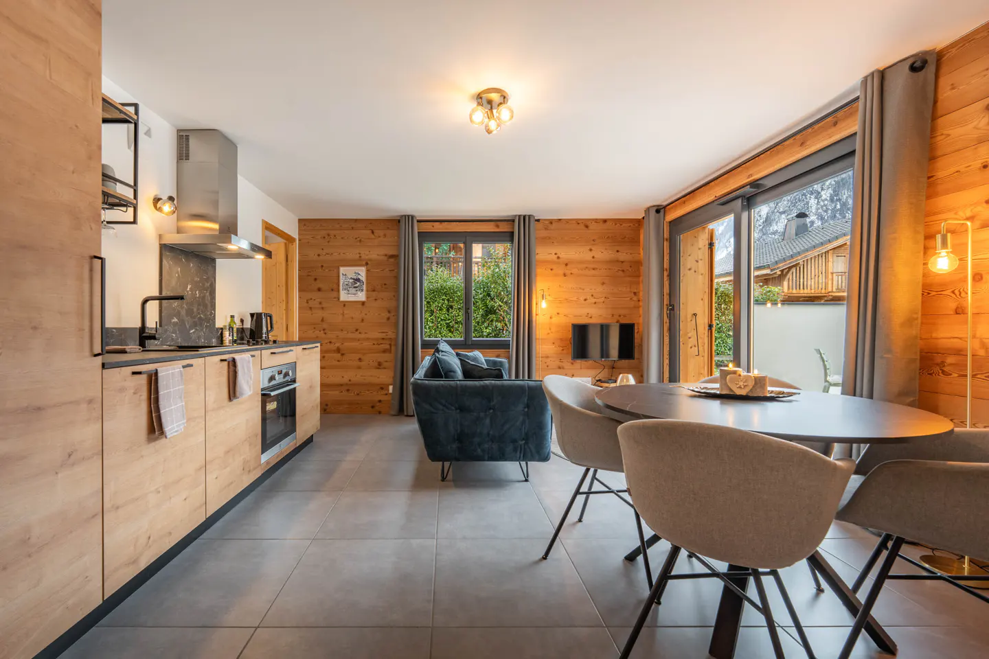 Interior view of a modern apartment with wood paneled walls, a kitchen, a blue sofa, and a dining table with chairs.