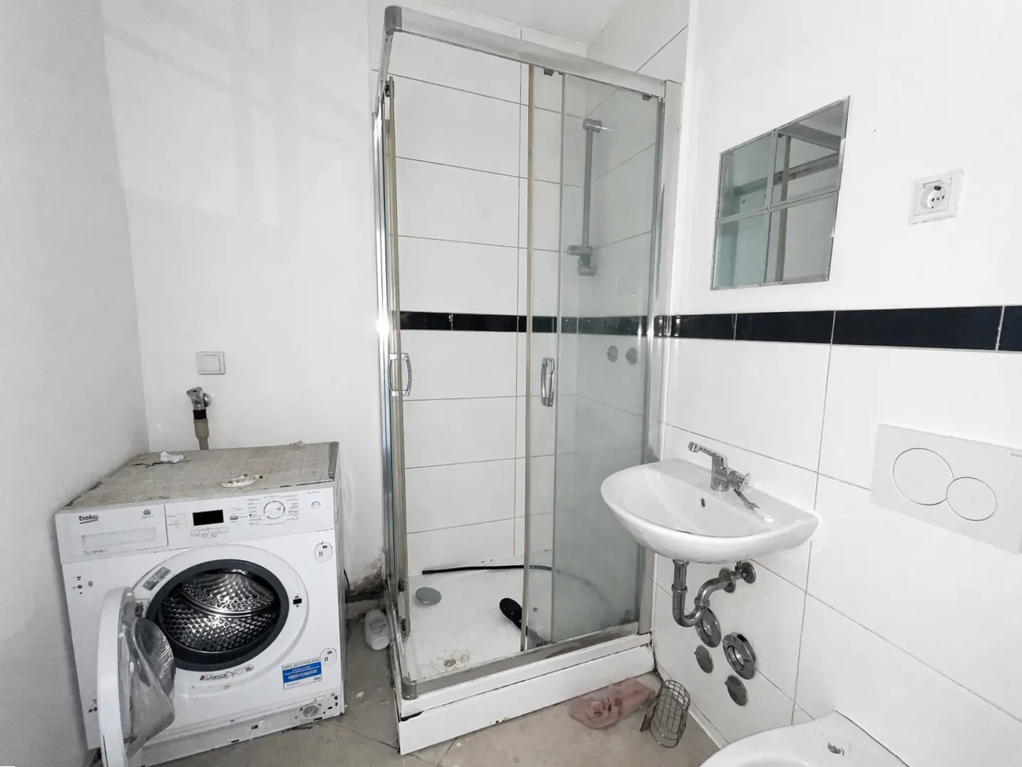 Bathroom with a white washing machine, a glass shower stall, and a white sink with a mirror above.