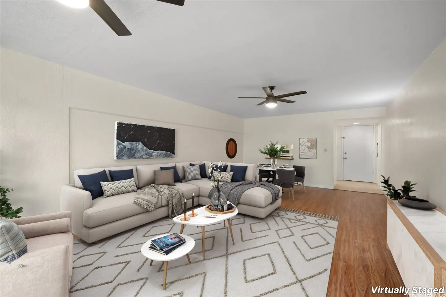 Living room with a beige sectional sofa, blue pillows, and a geometric rug. A dining table and chairs are visible in the background.