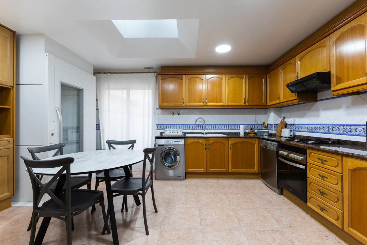 Kitchen with wooden cabinets, tiled backsplash, built-in appliances, and a round dining table with four black chairs.