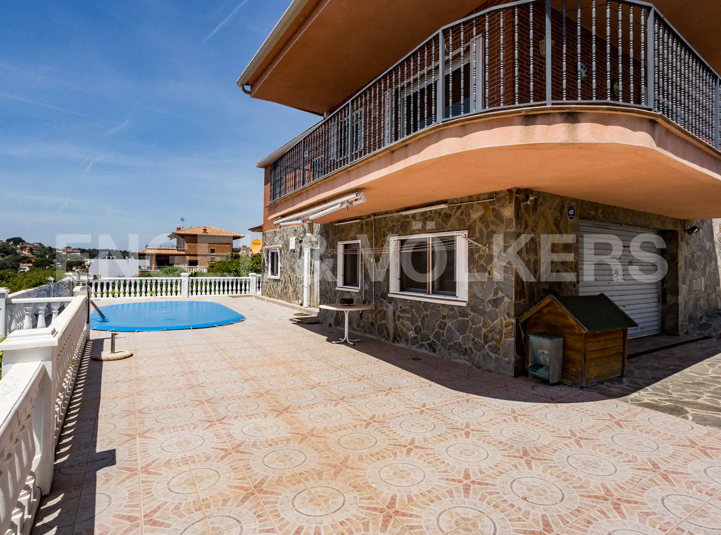 Two-story house with stone facade, balcony, and tiled patio. A blue-covered pool and dog house are visible.