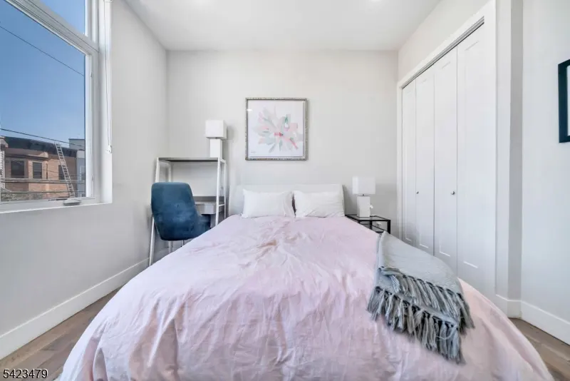 Bright bedroom with pink bedding, white walls, and a blue chair by a desk. A gray throw blanket is on the bed.