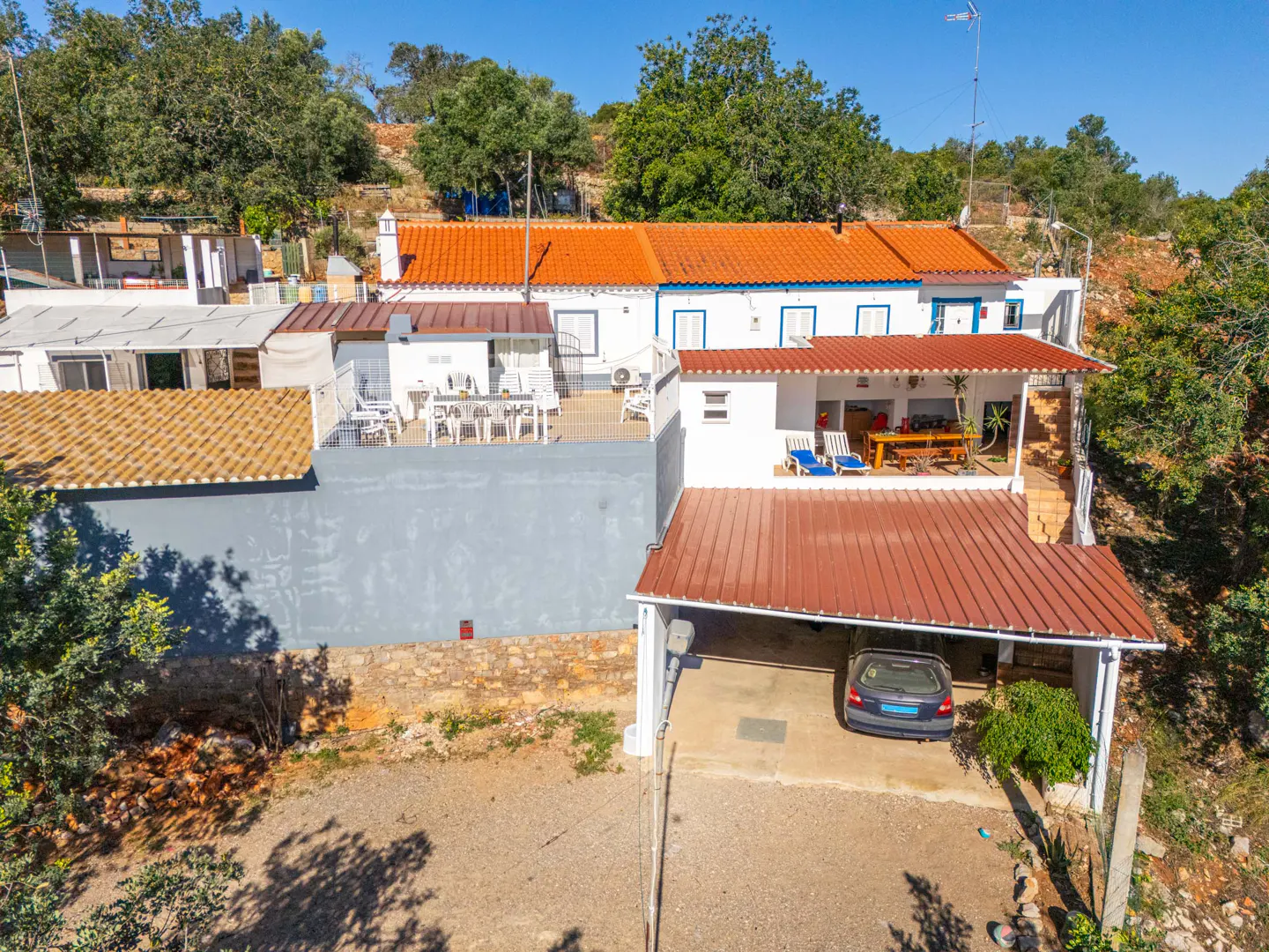 Aerial view of a white house with an orange roof, a carport with a blue car, and outdoor seating areas.