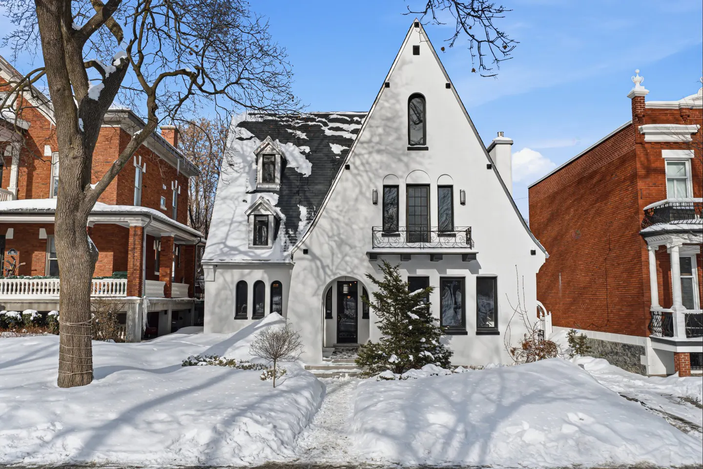 Exterior view of a white Tudor-style house with a black roof, surrounded by snow-covered ground and bare trees.